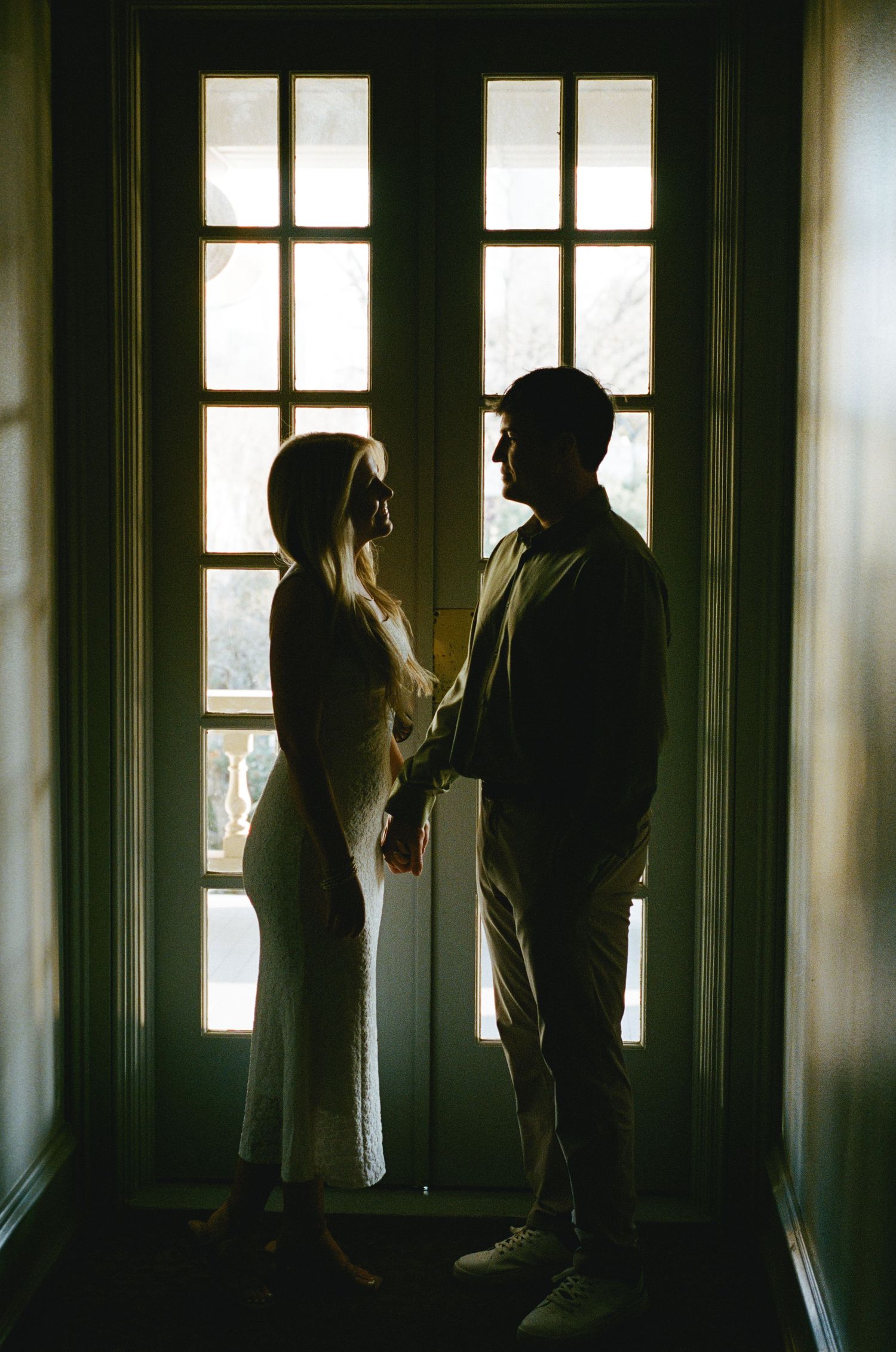 Silhouette of a couple holding hands facing each other in front of French doors with soft backlight.