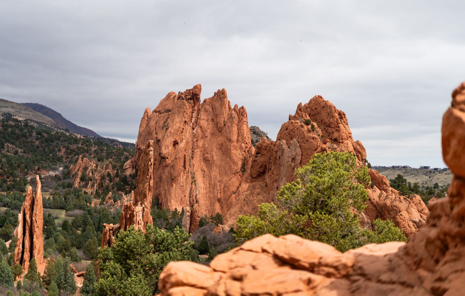 Dramatic red rock formations at Garden of the Gods Colorado Springs with cloudy sky and green trees.