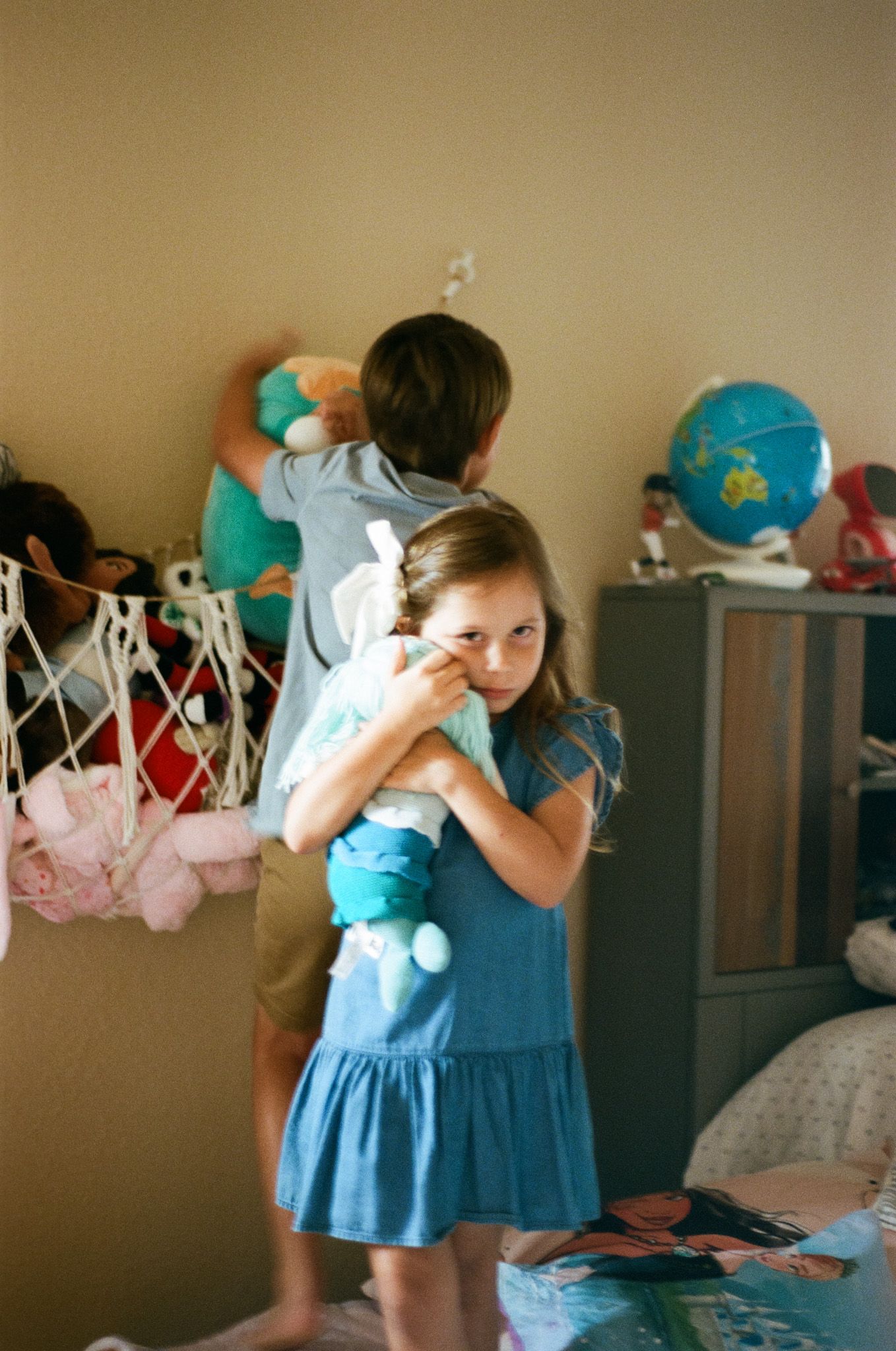 Young girl in blue dress hugging stuffed animal in colorful playroom.