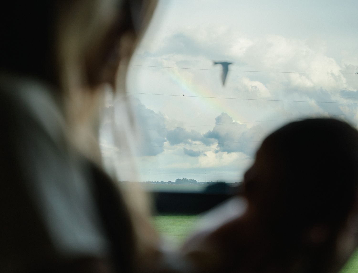 View through a window of a rainbow and clouds over a green field, with mother and baby silhouetted.