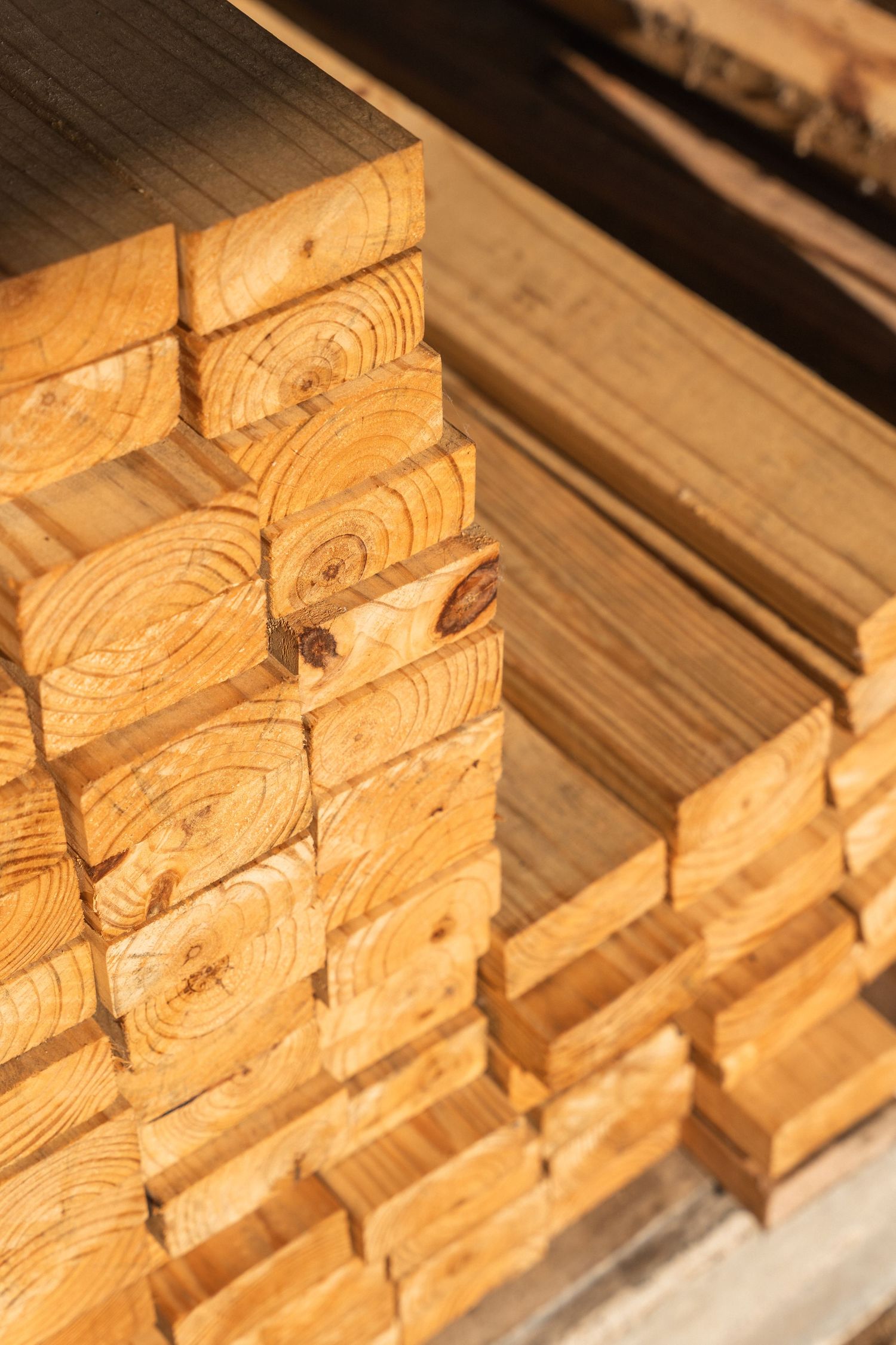 Stacked fresh-cut lumber planks showing natural wood grain rings at a construction supply yard.