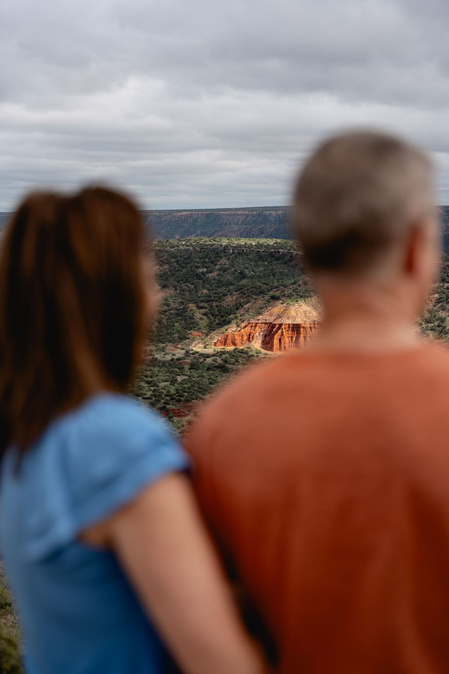 Couple standing at overlook admiring red rock canyon landscape under cloudy skies.