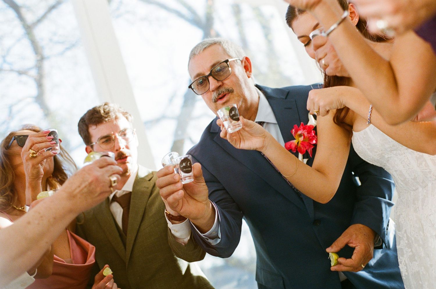 Wedding party group toasting together with shot glasses during a joyful outdoor celebration.
