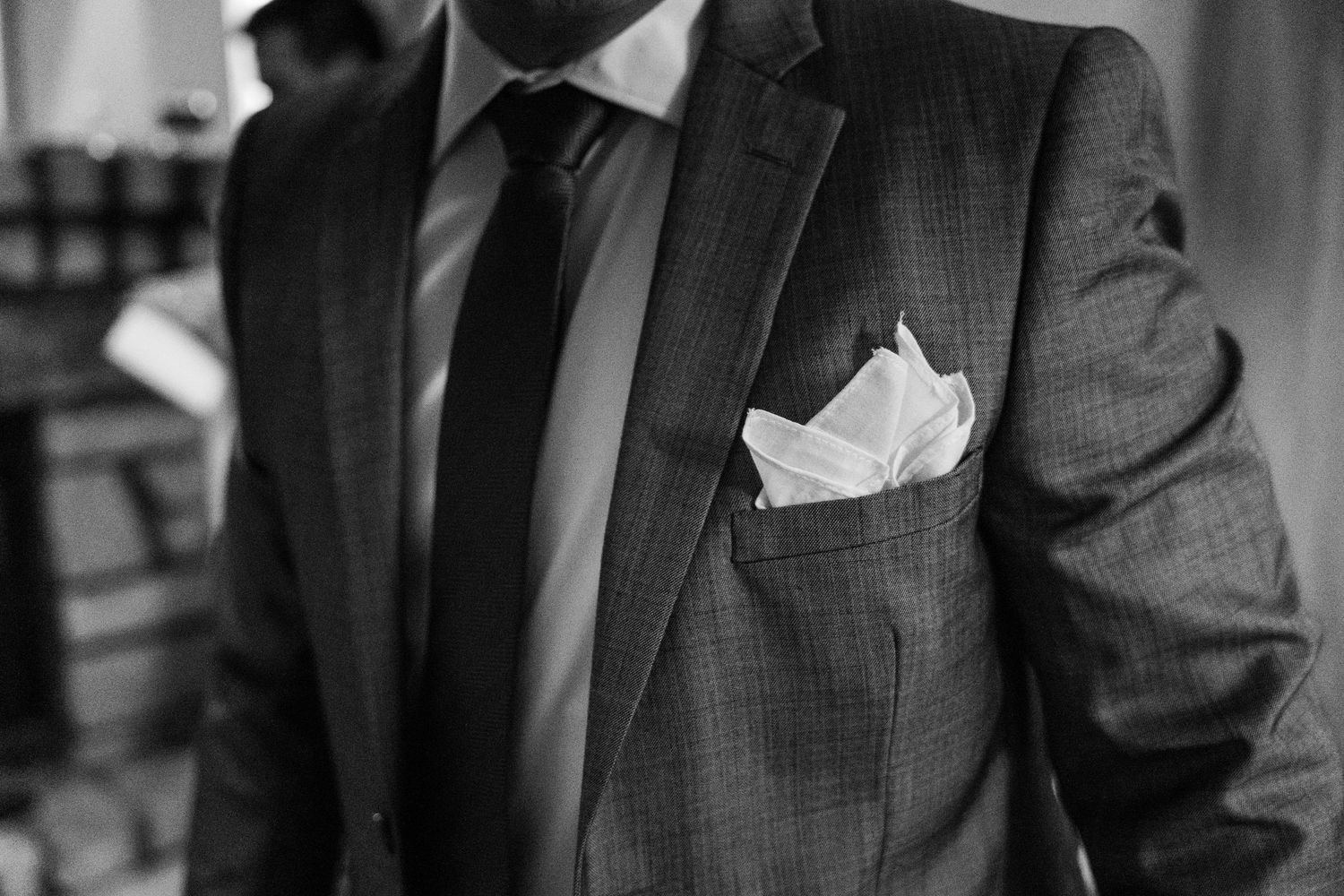 Black and white close-up of groom in tailored suit with white pocket square.
