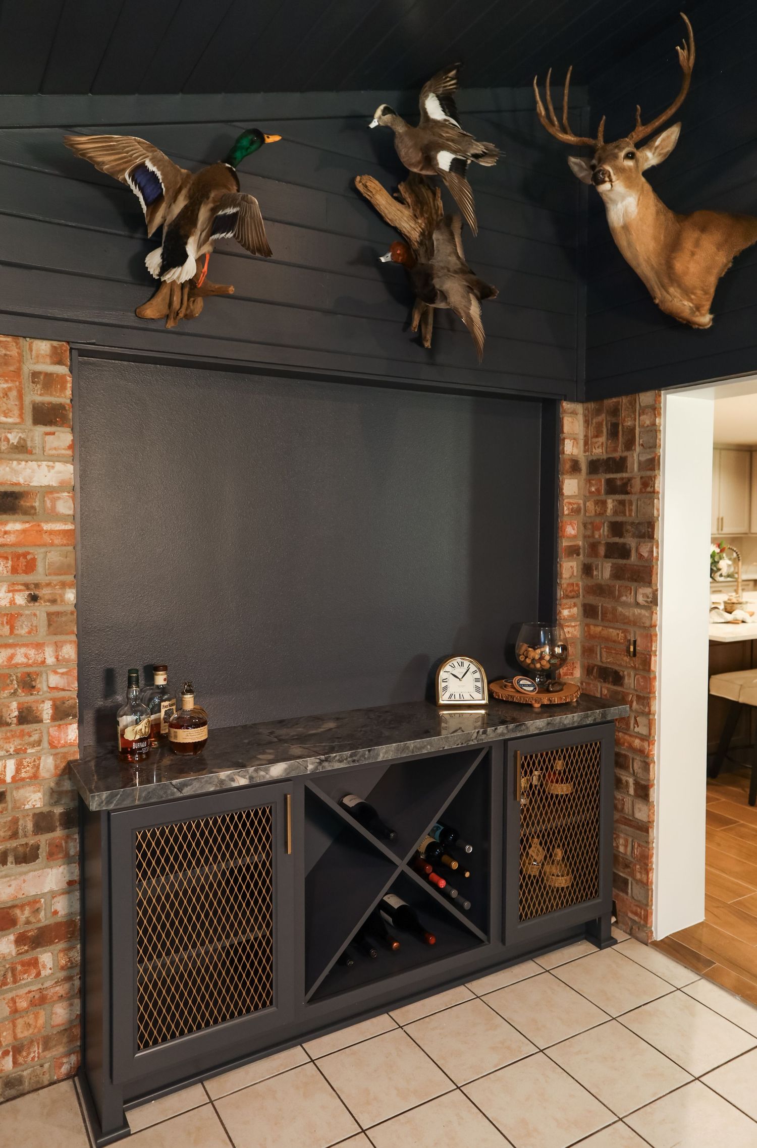 Rustic bar cabinet with wine rack, granite top, and taxidermy duck and deer mounts on dark wood-paneled wall.