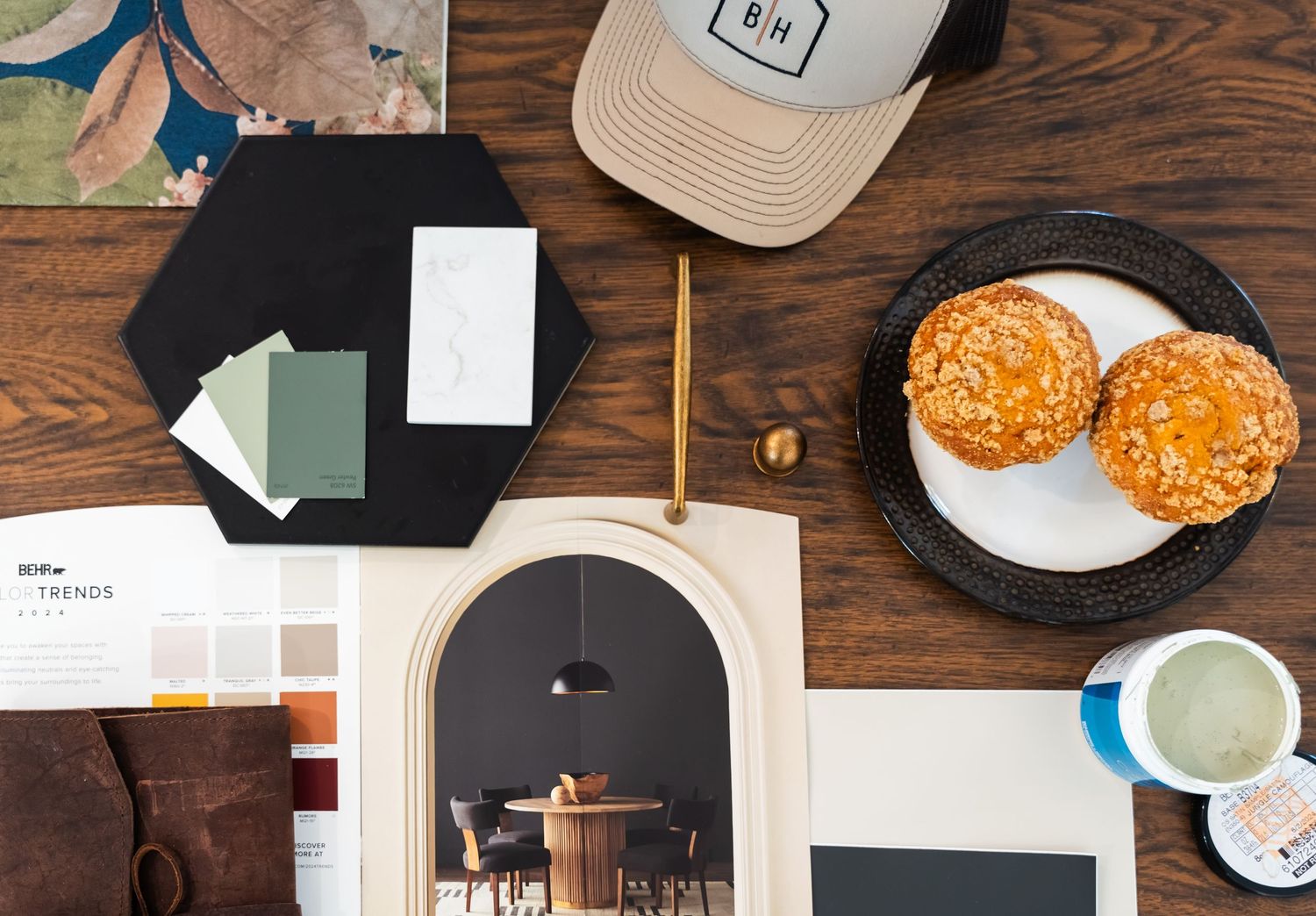 A flat lay of interior design materials including paint swatches, fabric samples, a magazine, and pastries.
