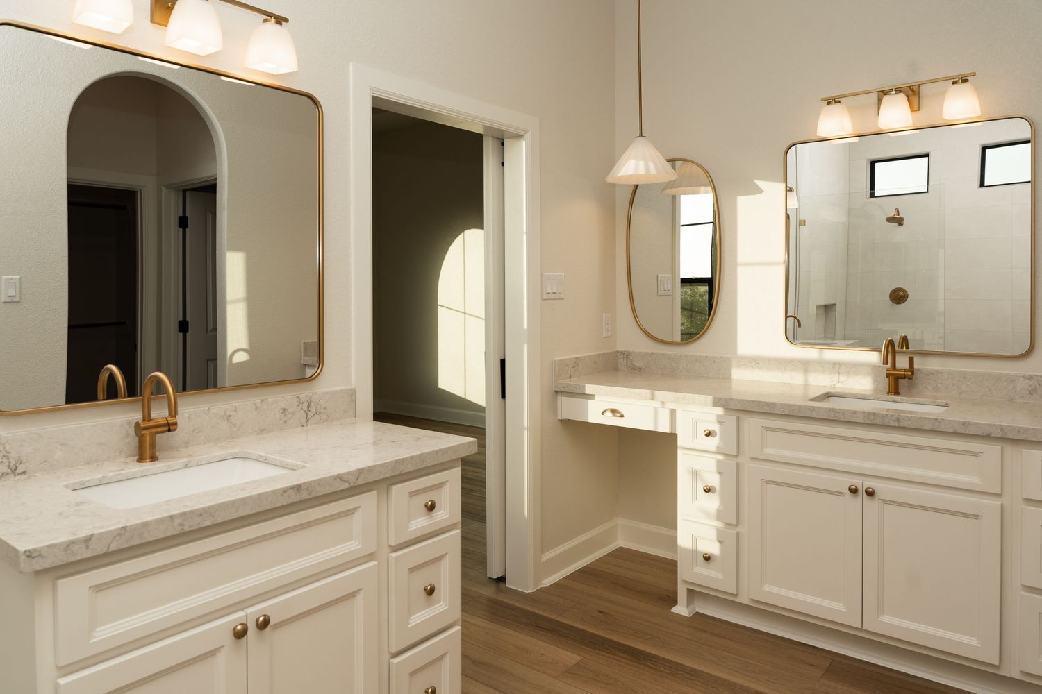 Elegant white bathroom with dual vanities, marble countertops, gold fixtures, arched mirrors, and hardwood floors.