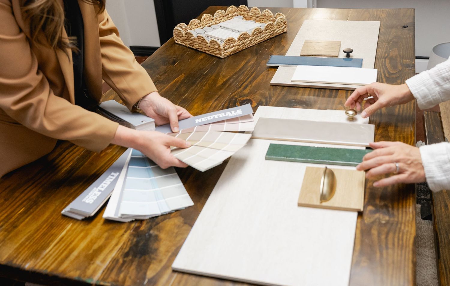 Two people reviewing paint swatches and material samples on a wooden desk during an interior design consultation.