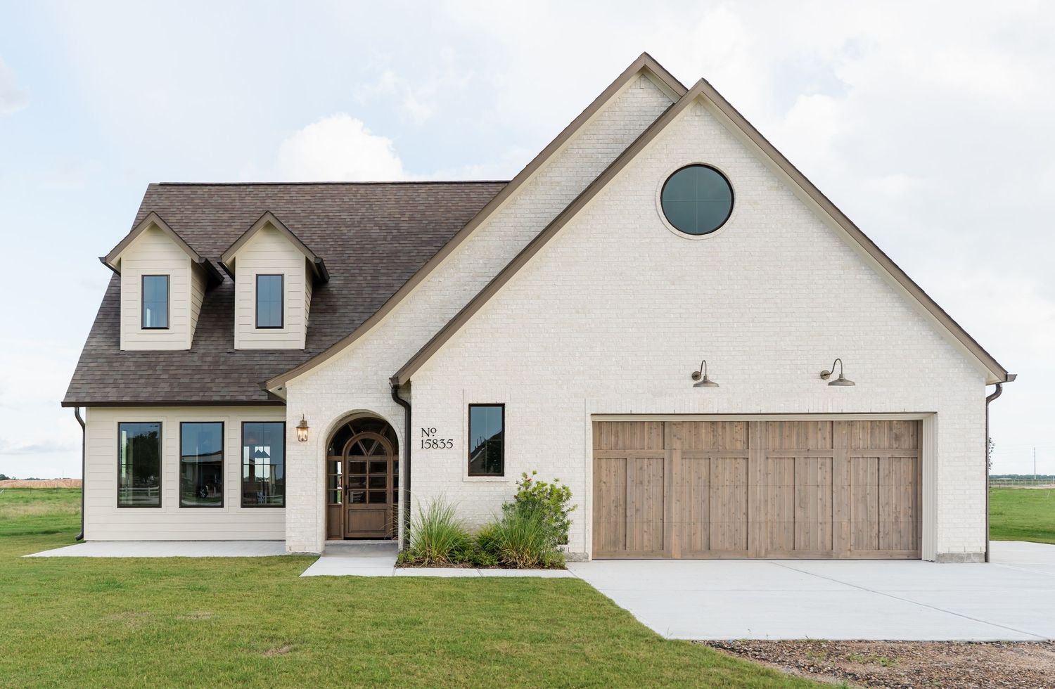 White painted brick modern farmhouse exterior with arched garage door, circular window, and dark shingled roof.