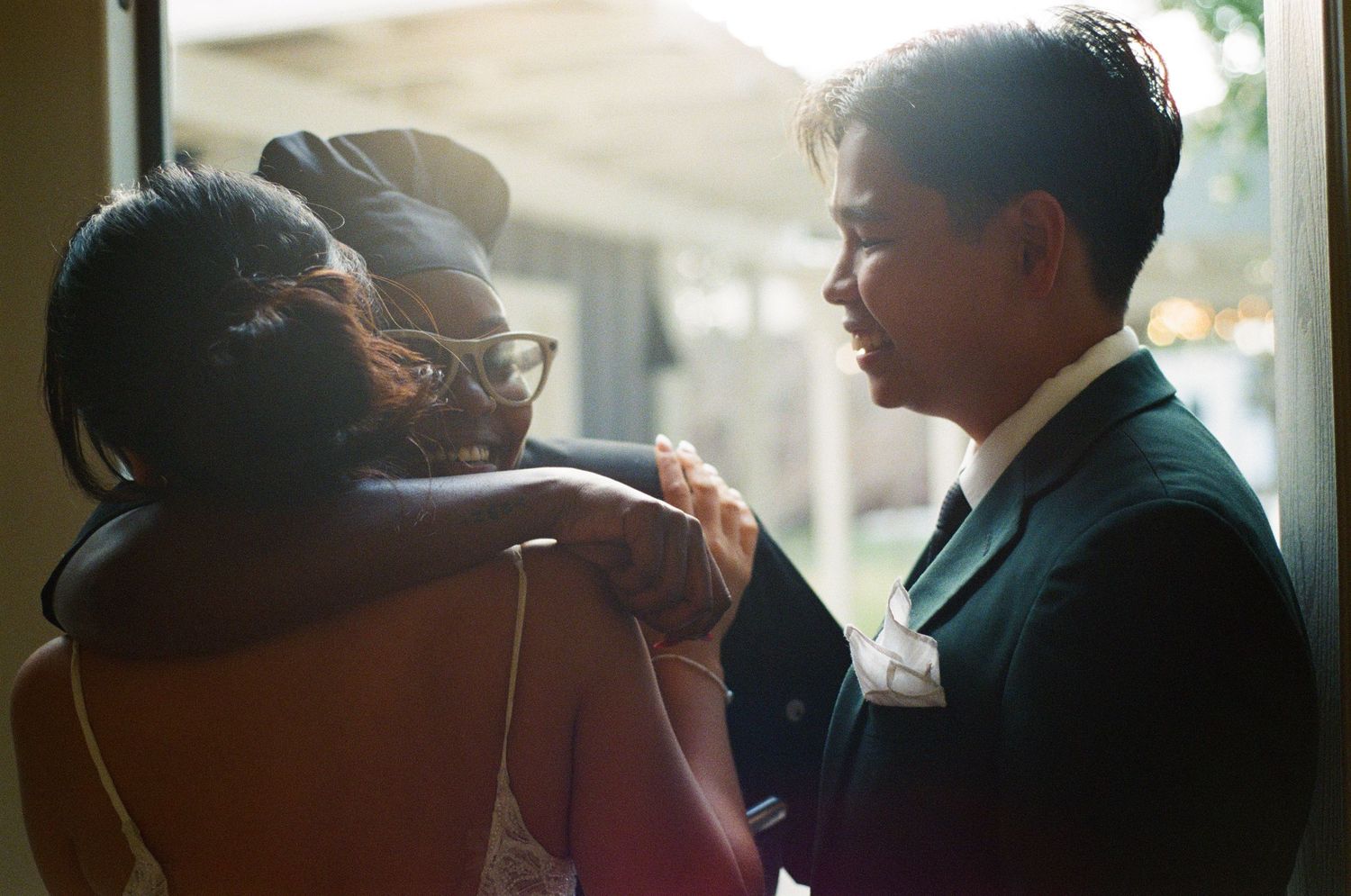 Emotional family embrace with groom comforting loved ones in soft backlit doorway.