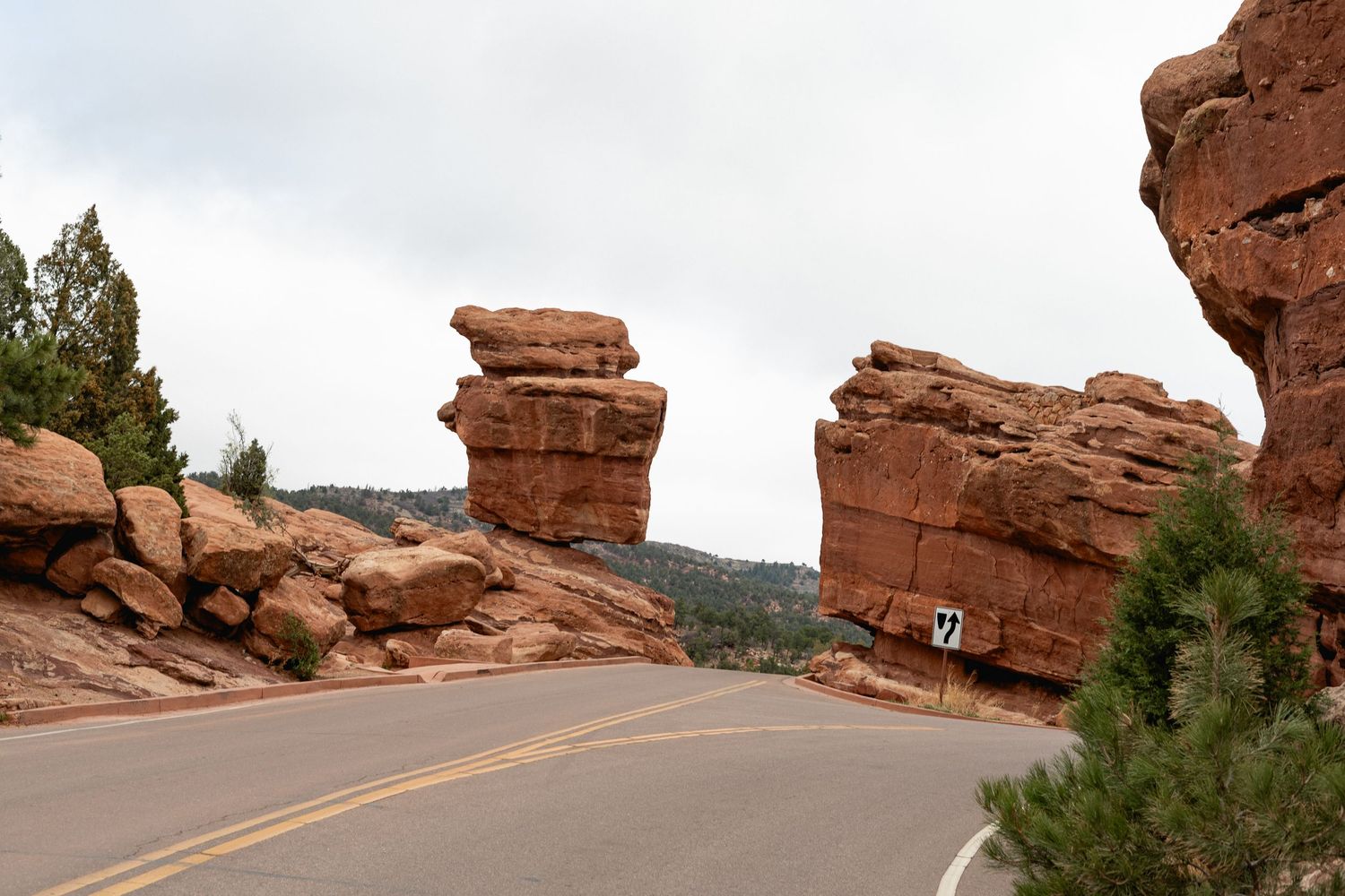 Curved road passing between towering red sandstone rock formations under cloudy skies in Garden of the Gods, Colorado.