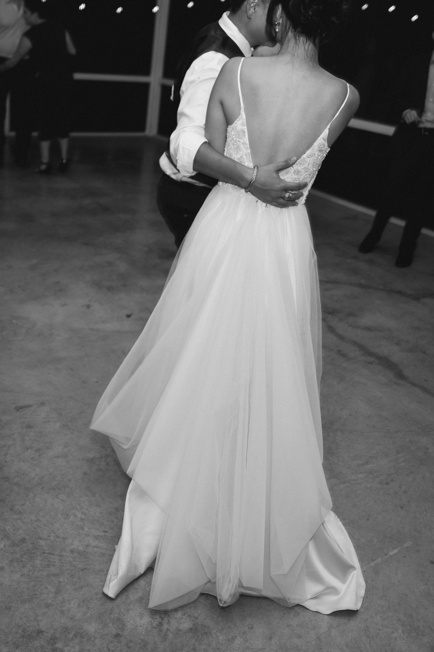 Elegant black and white photo of bride in backless gown dancing with groom at wedding reception.
