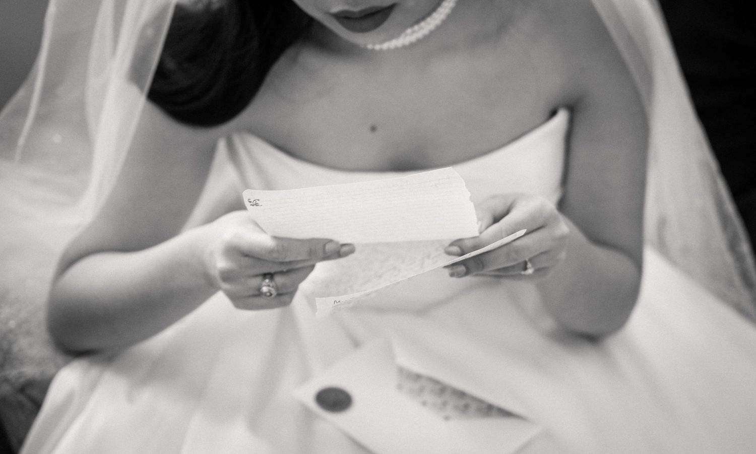 Black and white photo of bride in strapless gown reading a heartfelt letter before the ceremony.