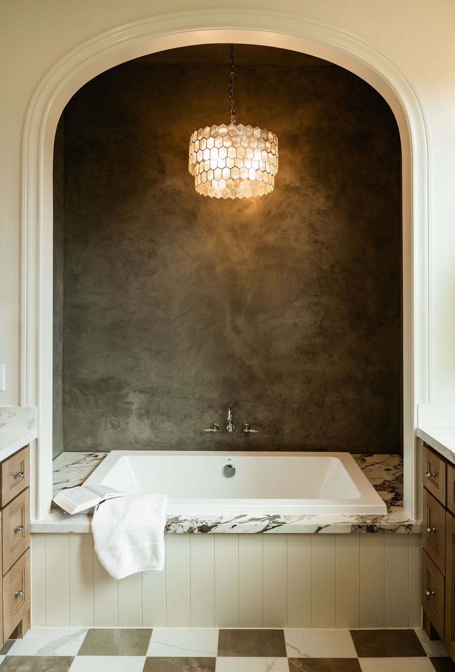Elegant bathroom niche with soaking tub, marble surround, capiz shell chandelier, and dark textured accent wall.