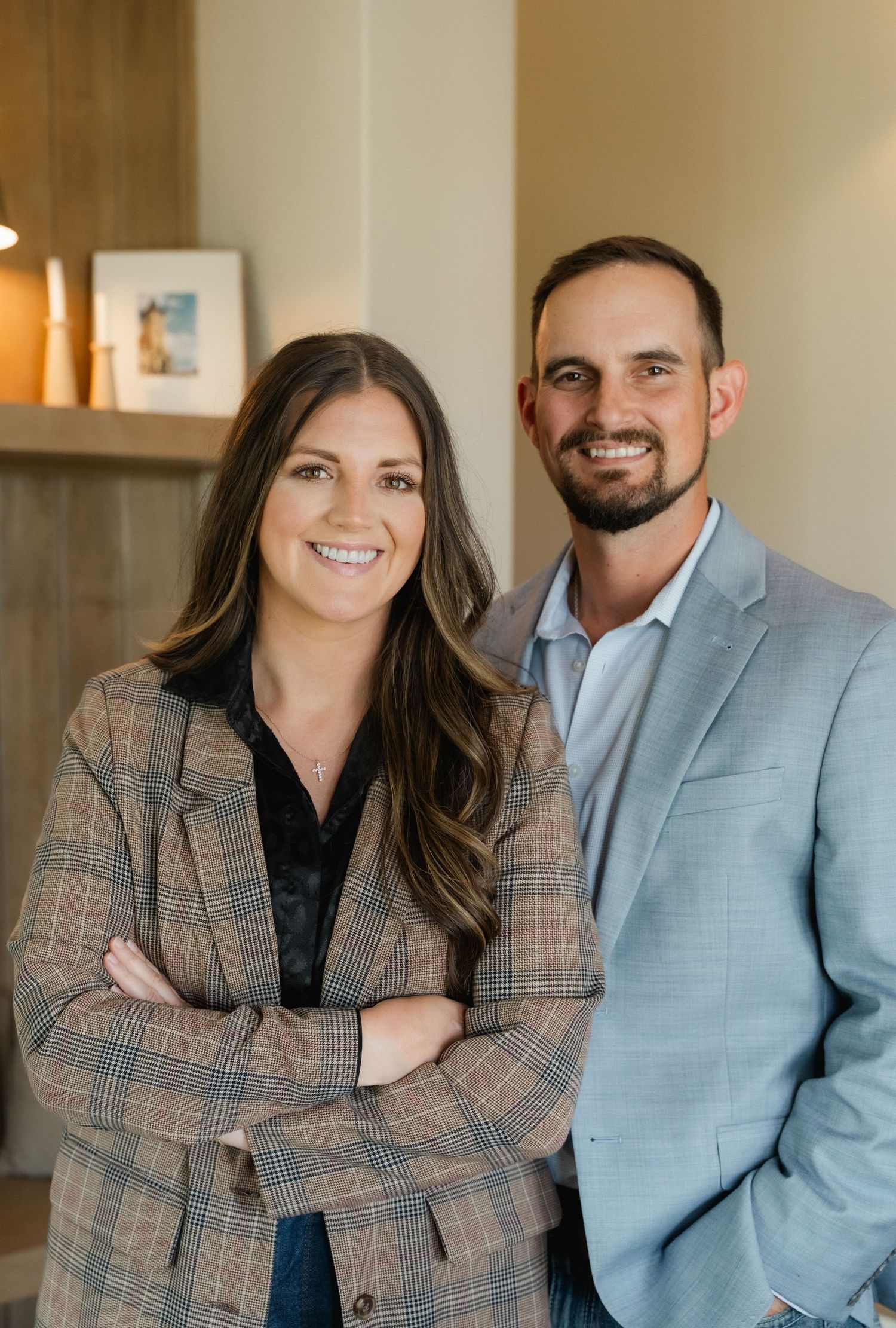 A smiling man and woman in professional blazers pose together indoors in a modern, well-lit space.