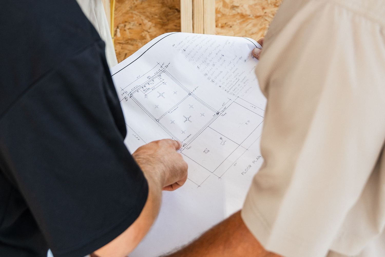 Two people reviewing architectural blueprints at a construction site with wooden framing visible in the background.