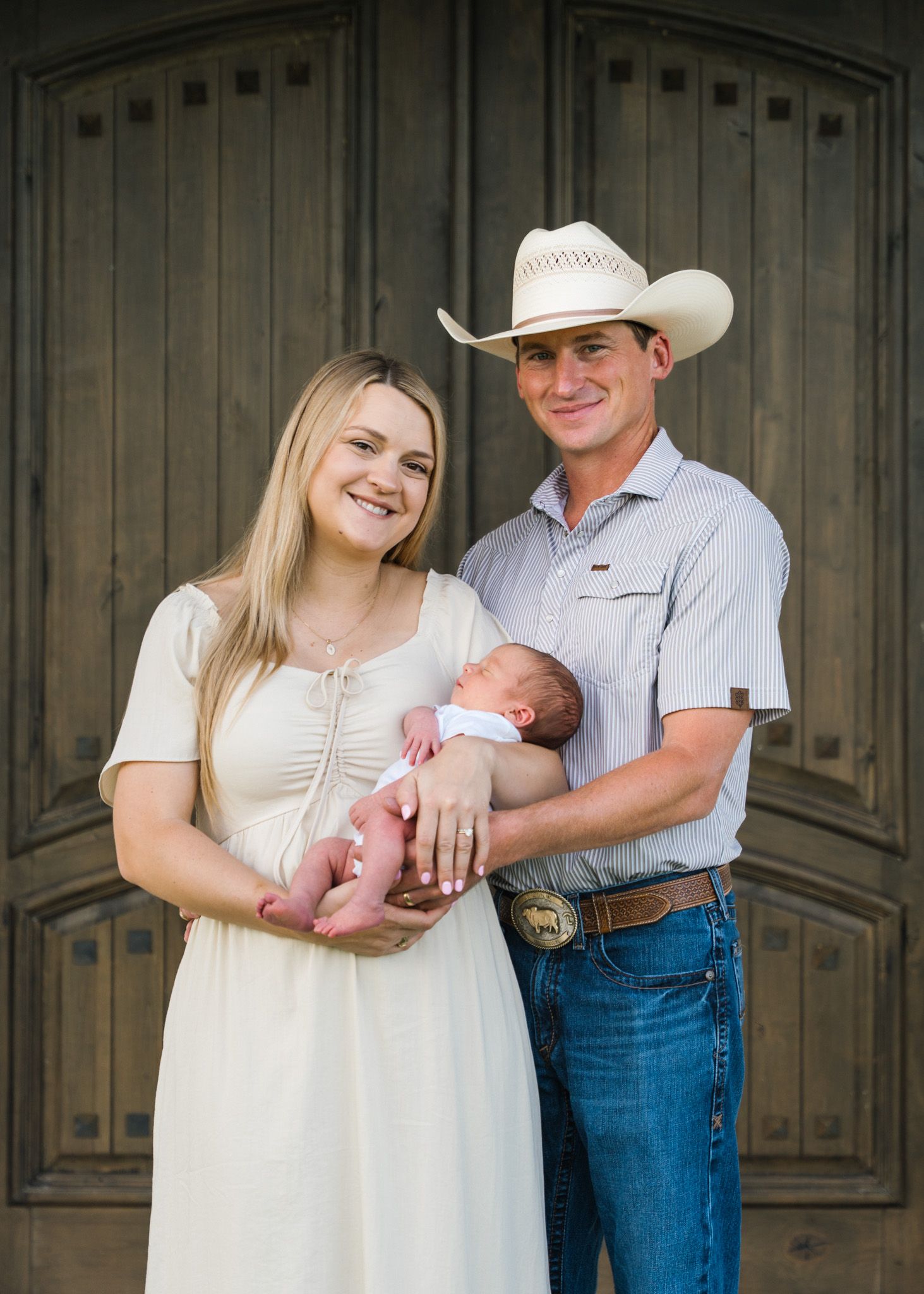 New parents holding their son on their front porch during newborn session in East Bernard, Texas.