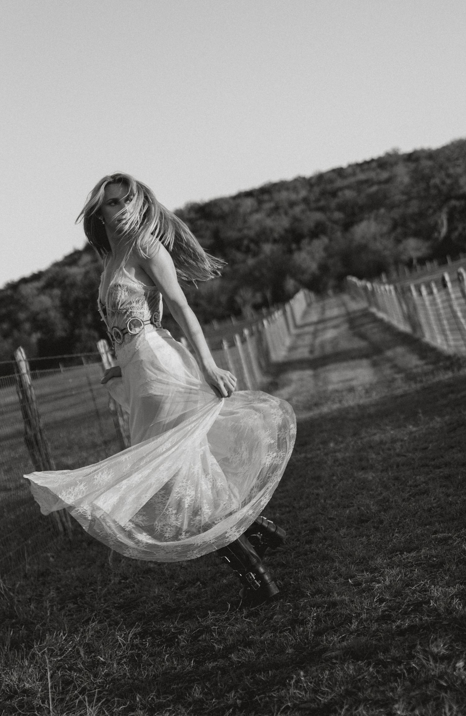 Woman in white lace dress spinning in field with hair flowing in black and white photo.