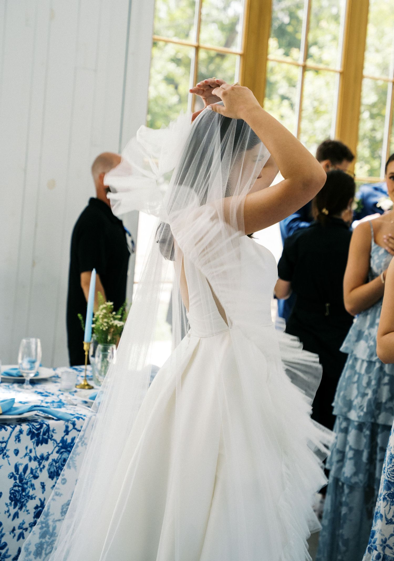 Bride in a fitted white gown adjusting her veil at a blue and white themed wedding reception.