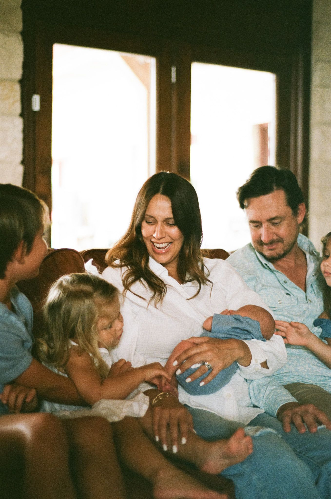 Happy family with newborn baby gathered on couch in warm sunlit home.