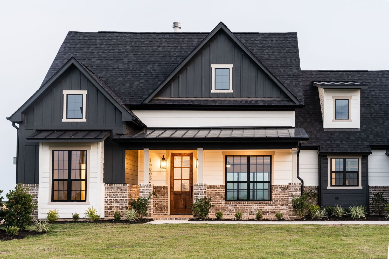 Modern farmhouse exterior with black siding, brick accents, dark roof, and manicured lawn.