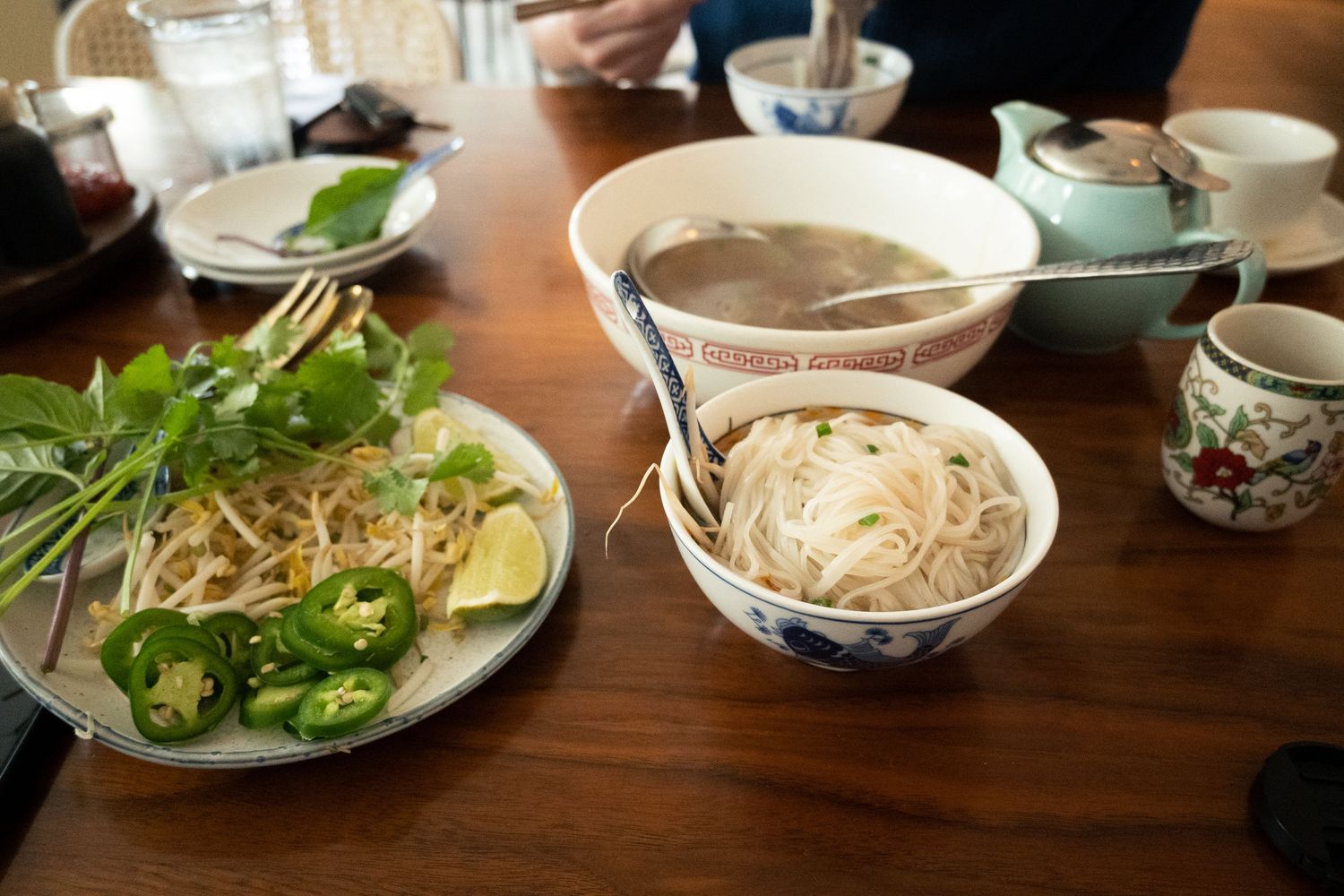 Bowl of Vietnamese pho with rice noodles served alongside a plate of fresh herbs, bean sprouts, jalapenos, and lime.