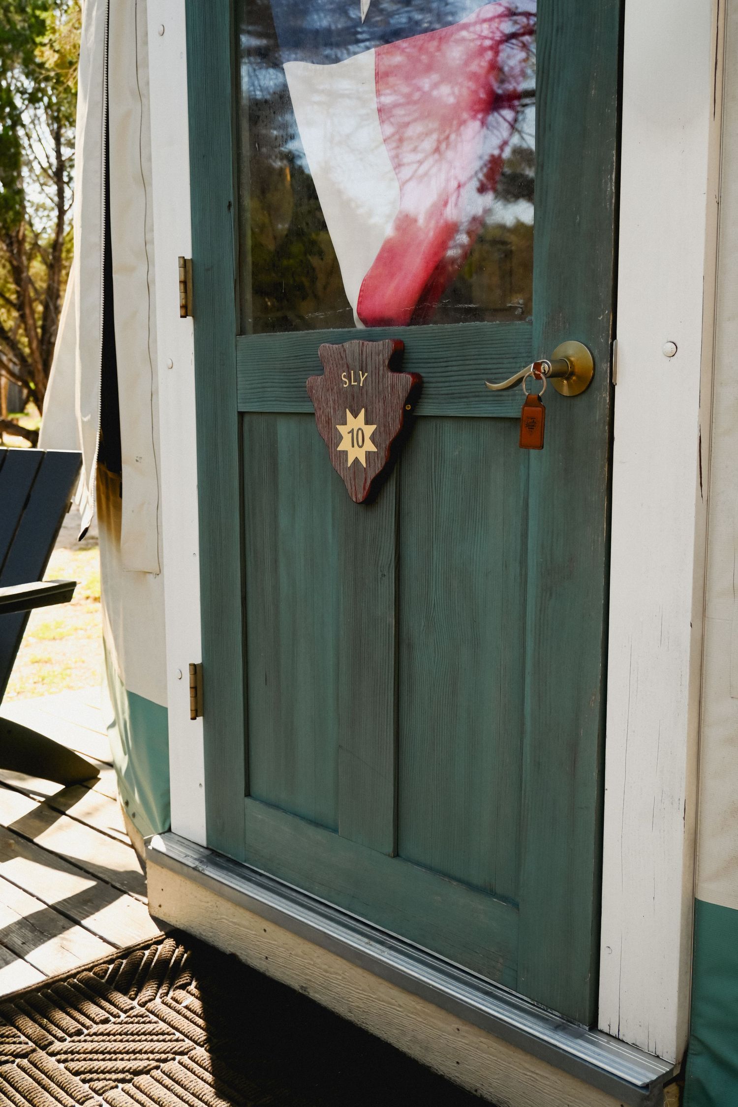Green Dutch door with Texas flag and arrowhead sign numbered 10 at a rustic yurt campsite.