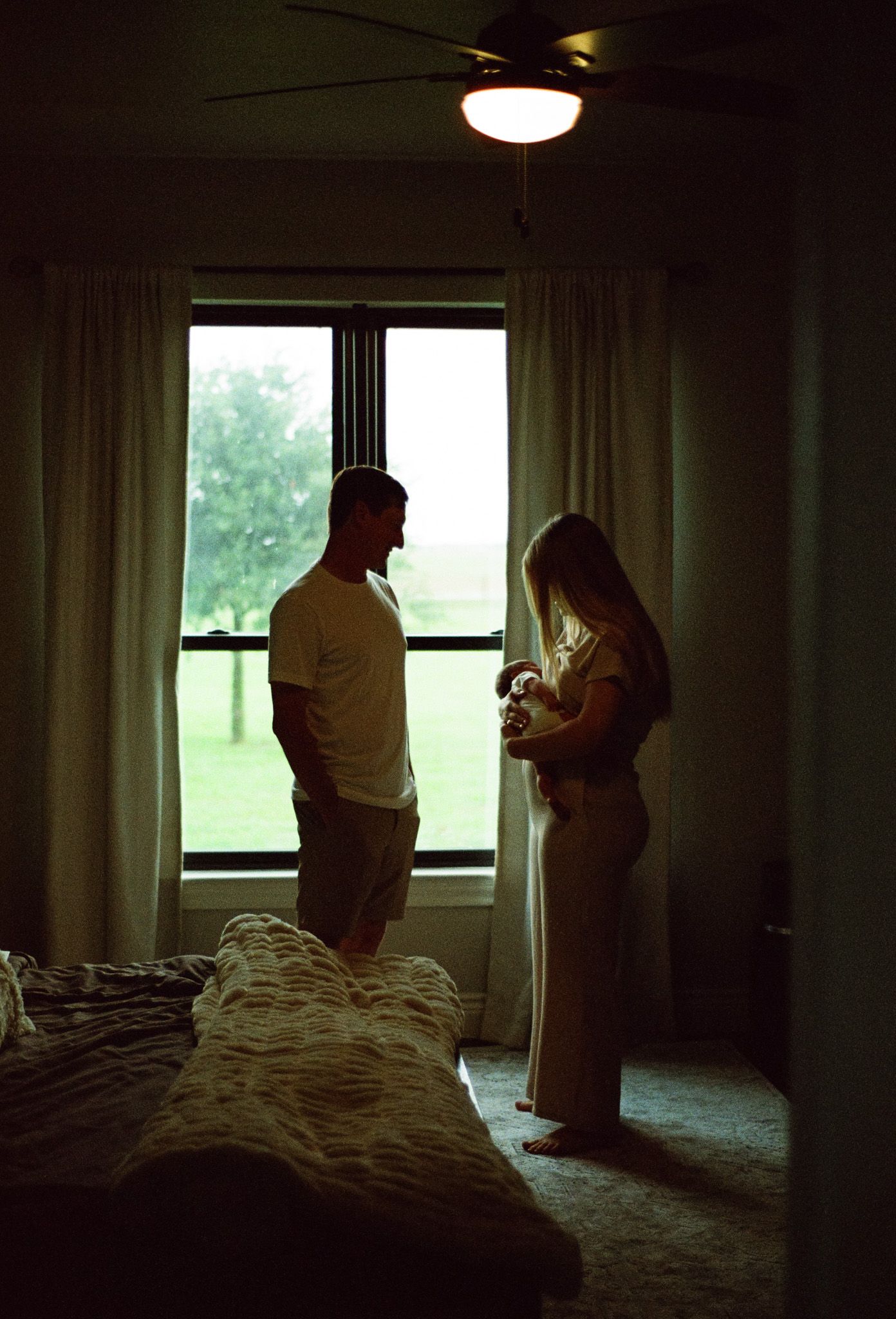 Silhouette of new parents holding their son in front of a window.