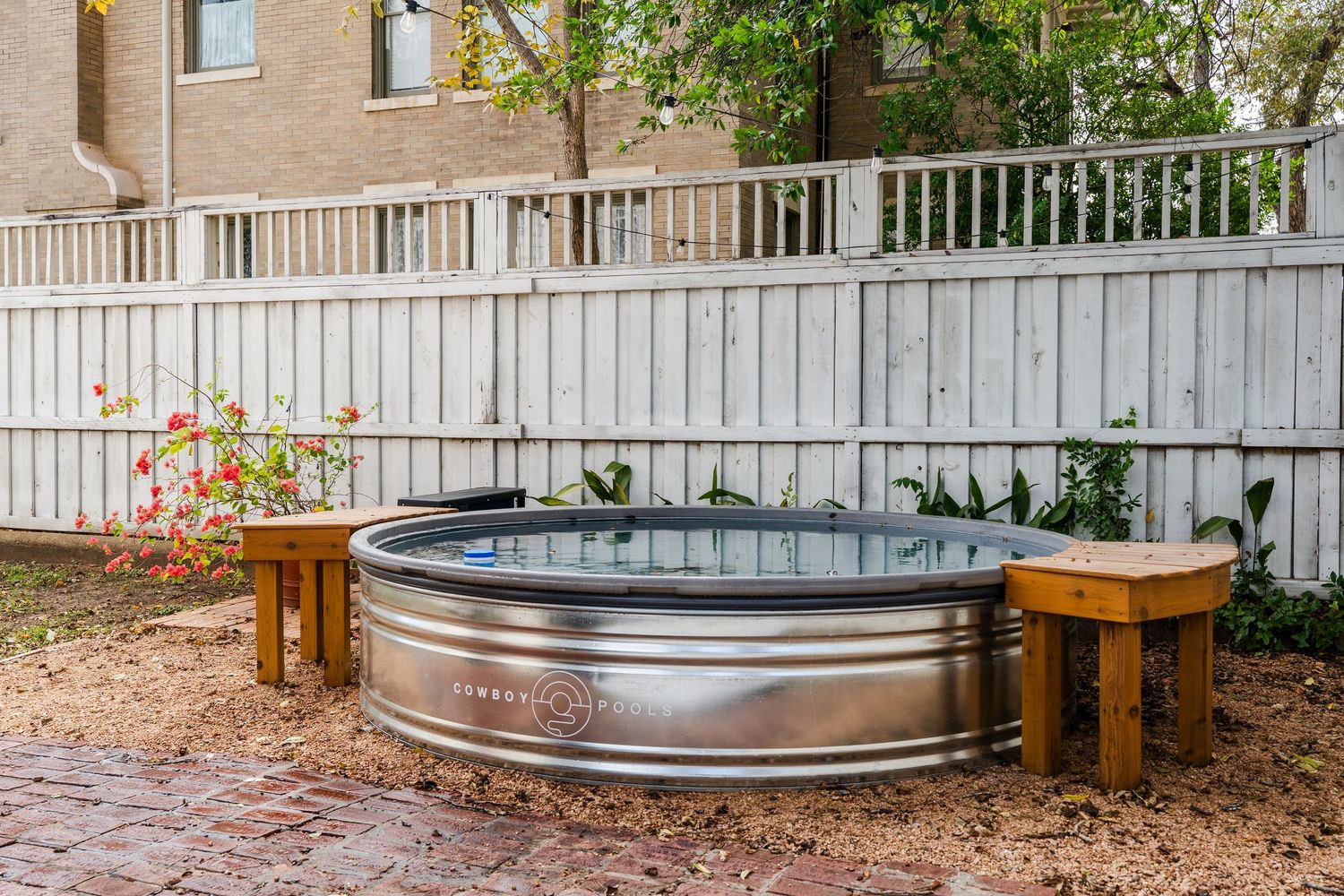 Galvanized steel stock tank cold plunge tub in backyard with wooden stools and white fence.