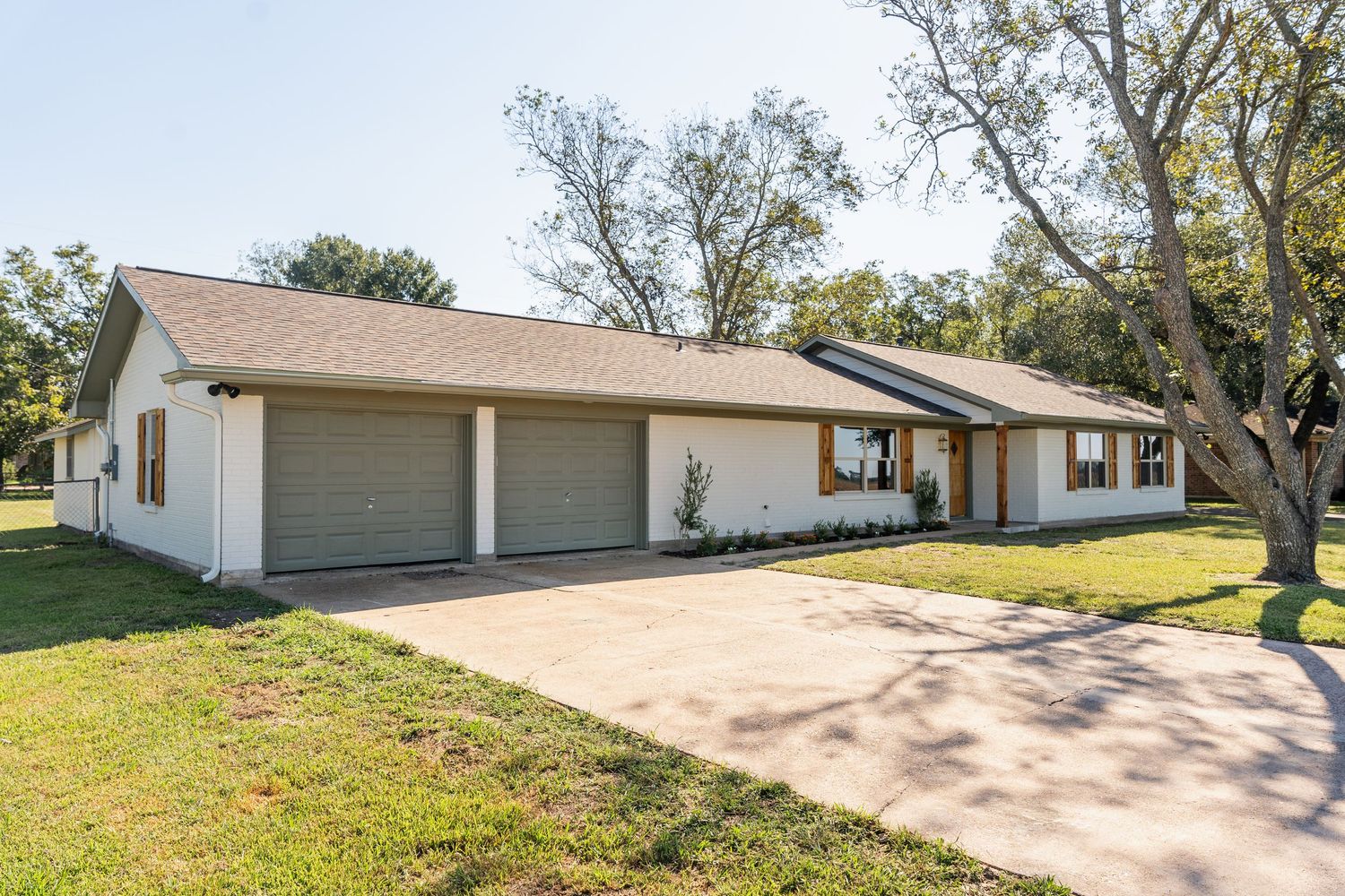 White ranch-style home with double garage, long driveway, and mature trees on a sunny day.
