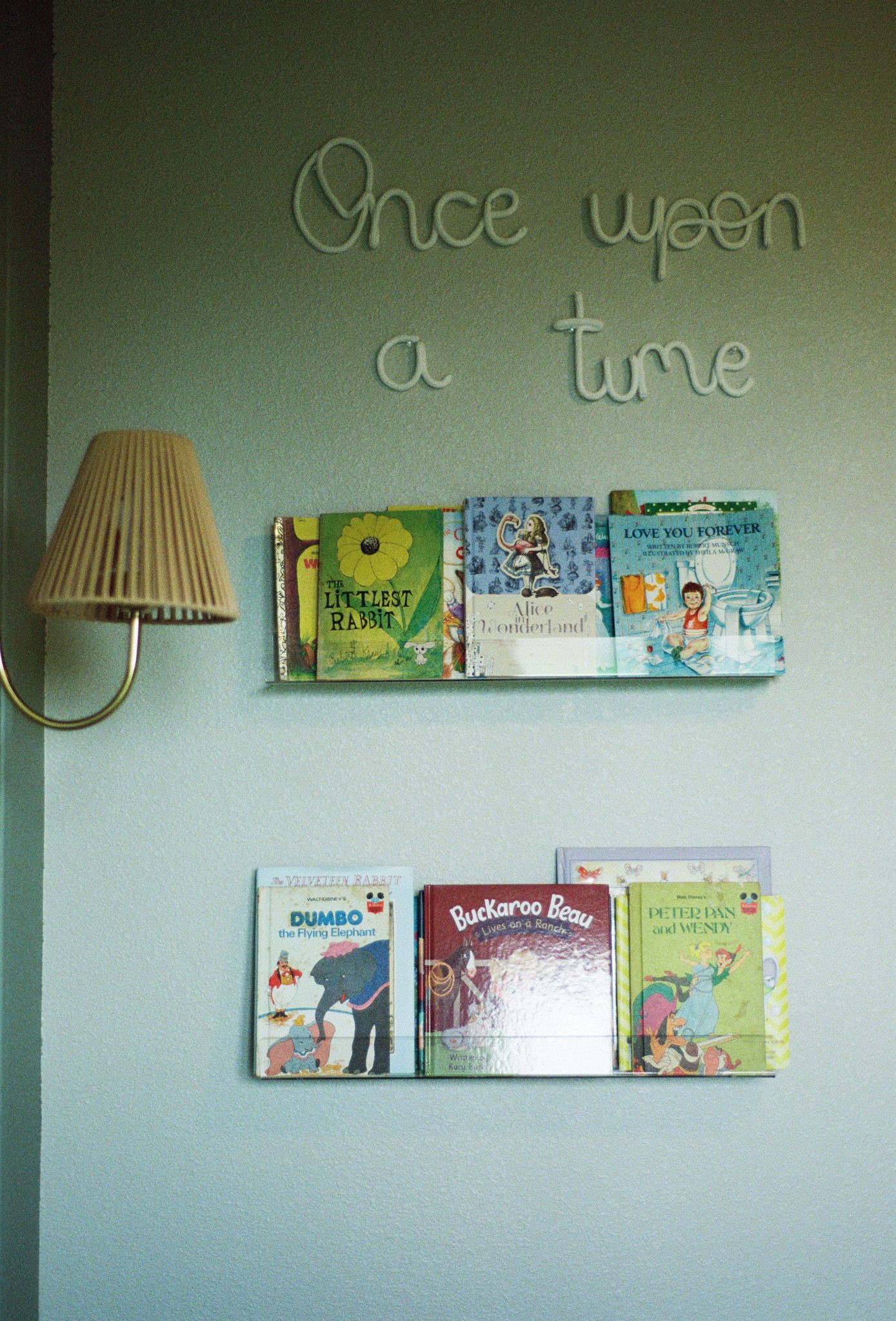 Sage green nursery wall with Once Upon a Time sign and vintage children's book display shelves.