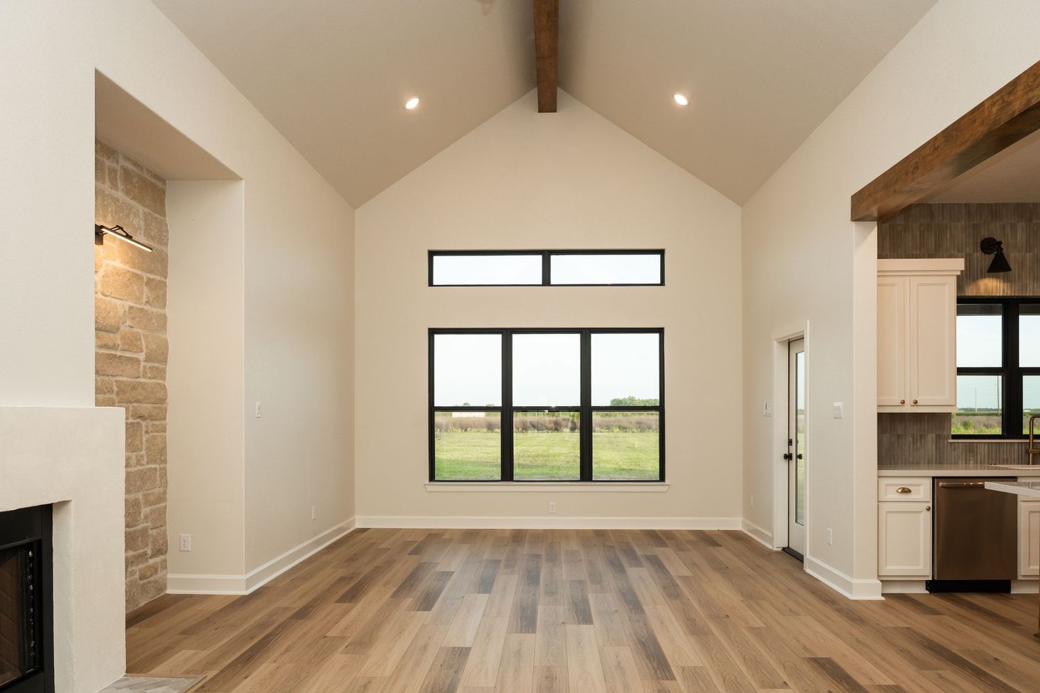 Spacious living room with vaulted ceilings, exposed wood beam, stone fireplace, and large black-framed windows.