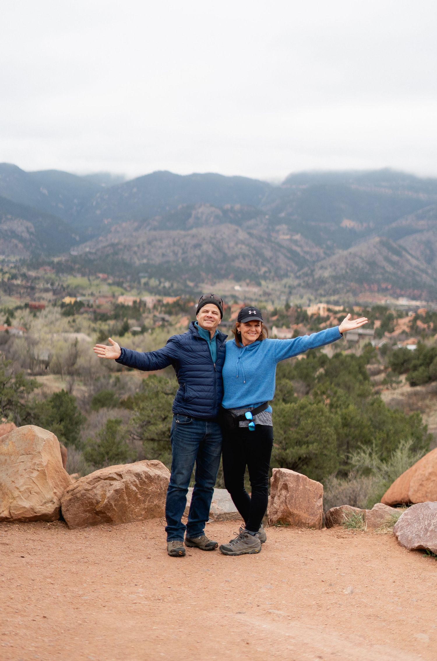 Couple posing with arms outstretched at Garden of the Gods overlook with stunning Colorado mountain views.