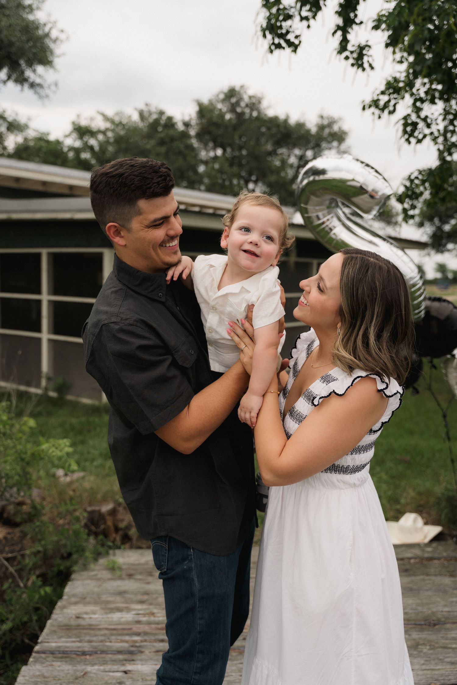 A happy young family with a baby boy celebrates outdoors with a silver balloon.