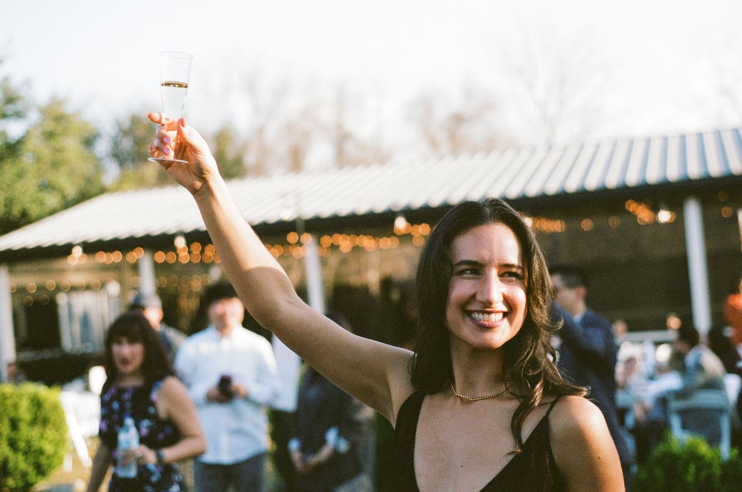 Smiling woman raising champagne glass at outdoor wedding reception.