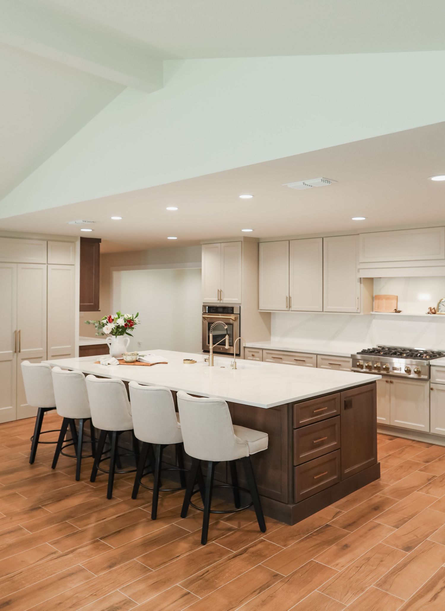 Modern open-concept kitchen with large island, white quartz countertops, bar stools, and wood-look tile flooring.