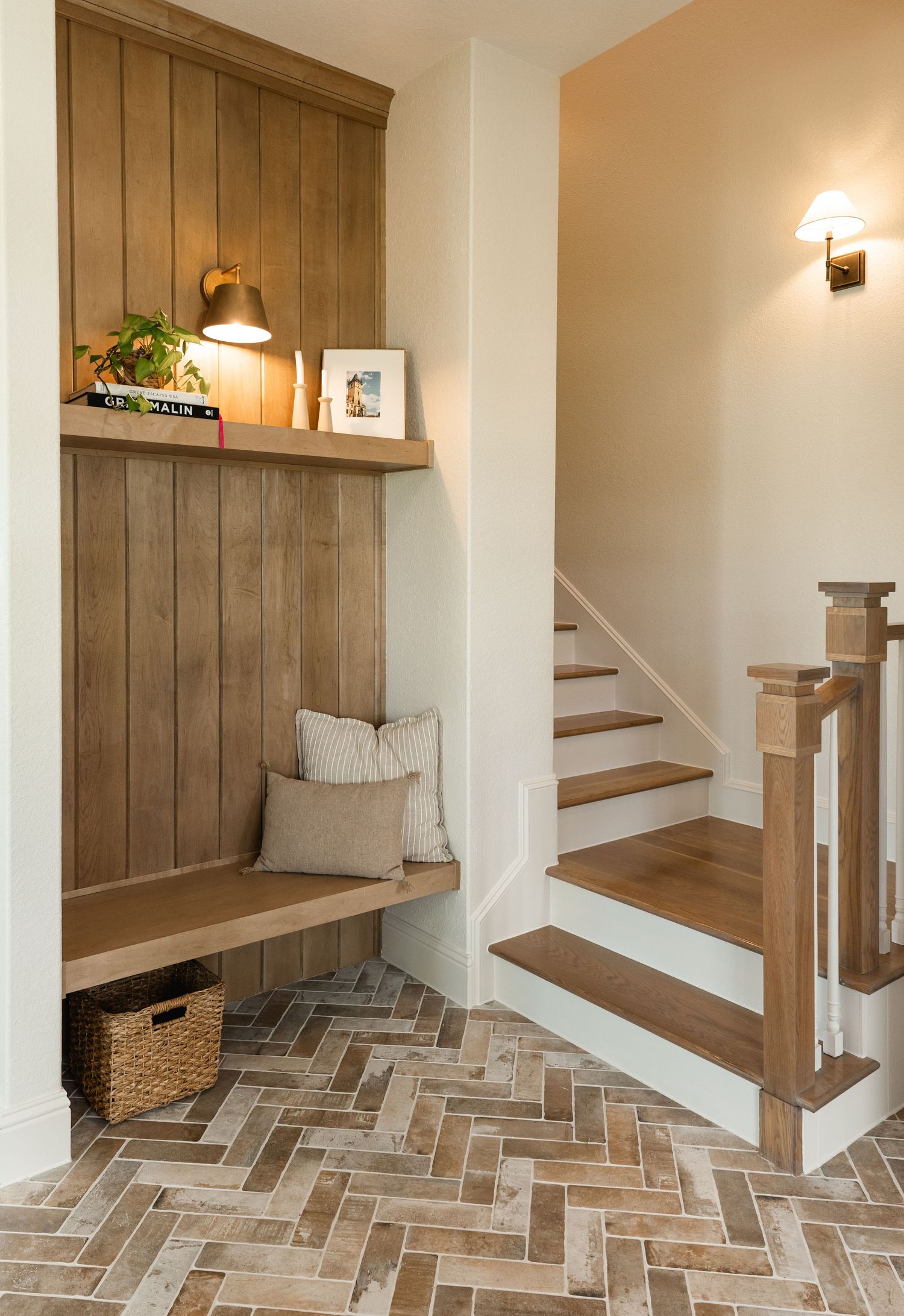Cozy mudroom bench with wood shiplap, herringbone brick floors, and staircase in a farmhouse home.