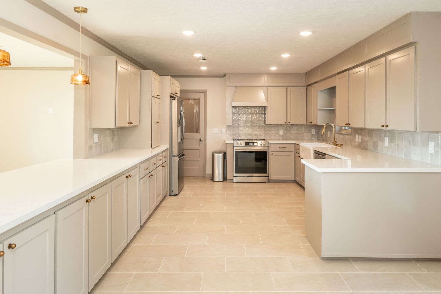 Renovated kitchen with gray shaker cabinets, white quartz countertops, stainless appliances, and tile backsplash.