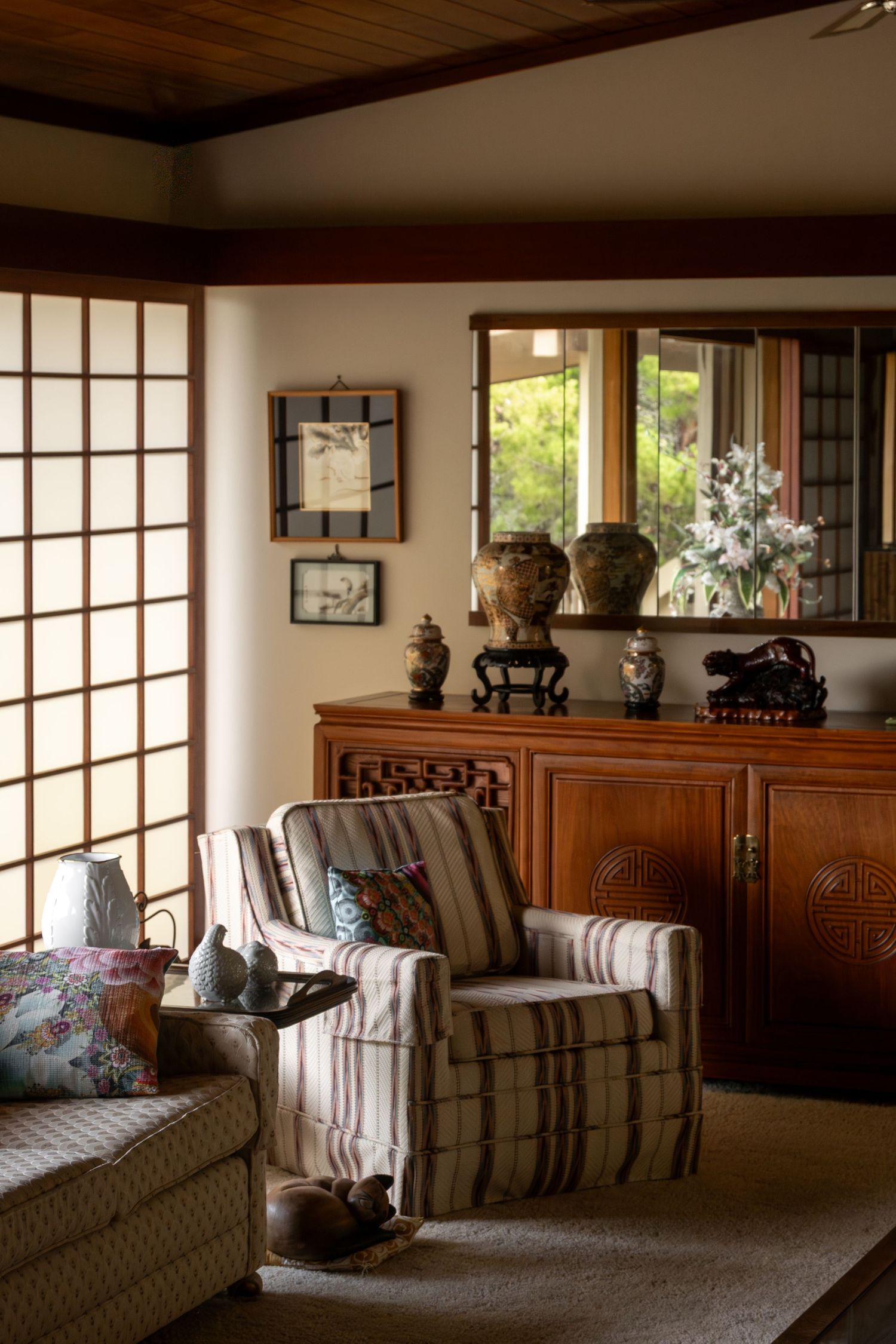 Japanese-inspired living room with shoji screens, striped armchair, wooden cabinet, decorative vases, and framed artwork.