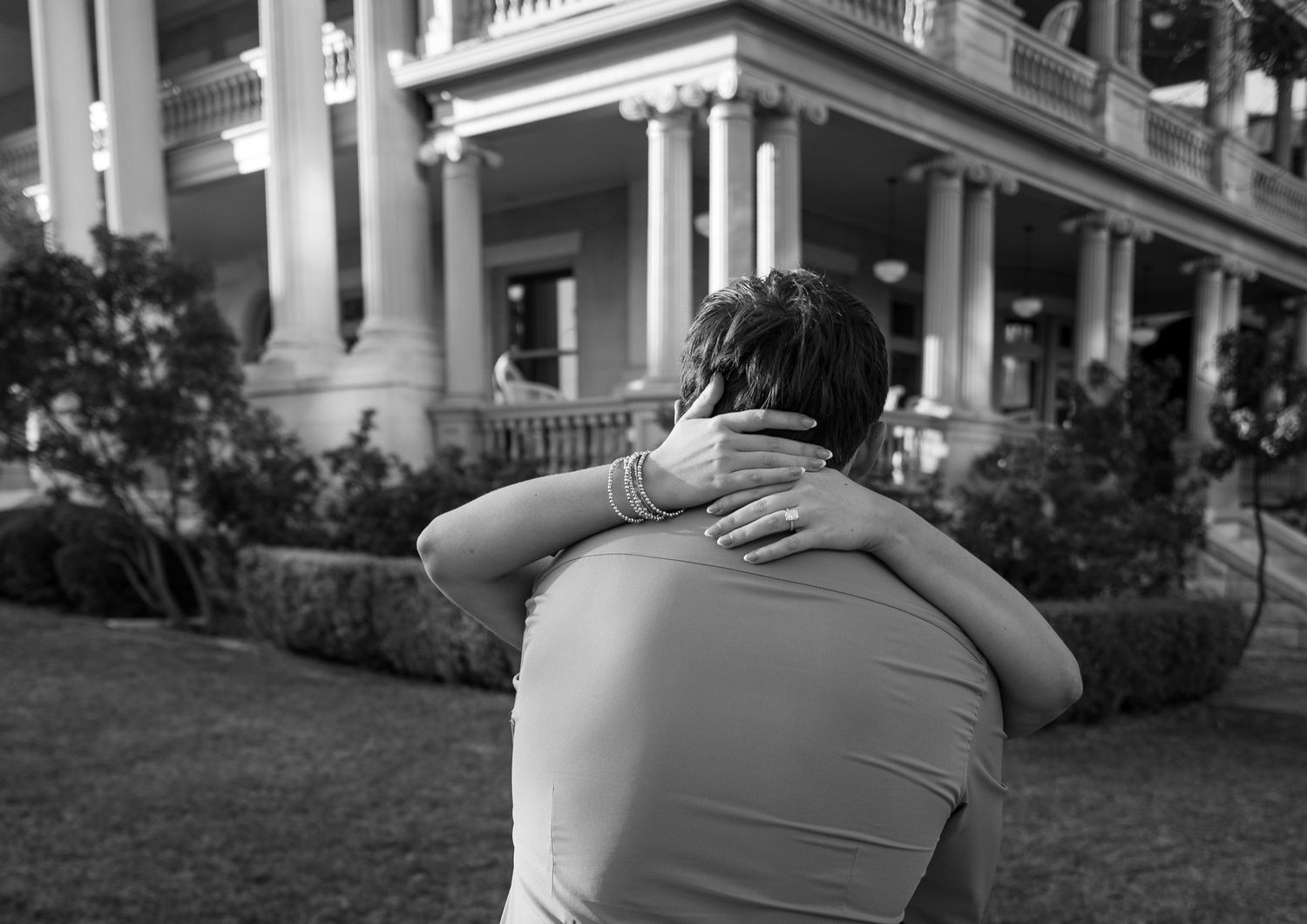 Black and white photo of two people embracing in front of a grand Southern mansion with white columns.