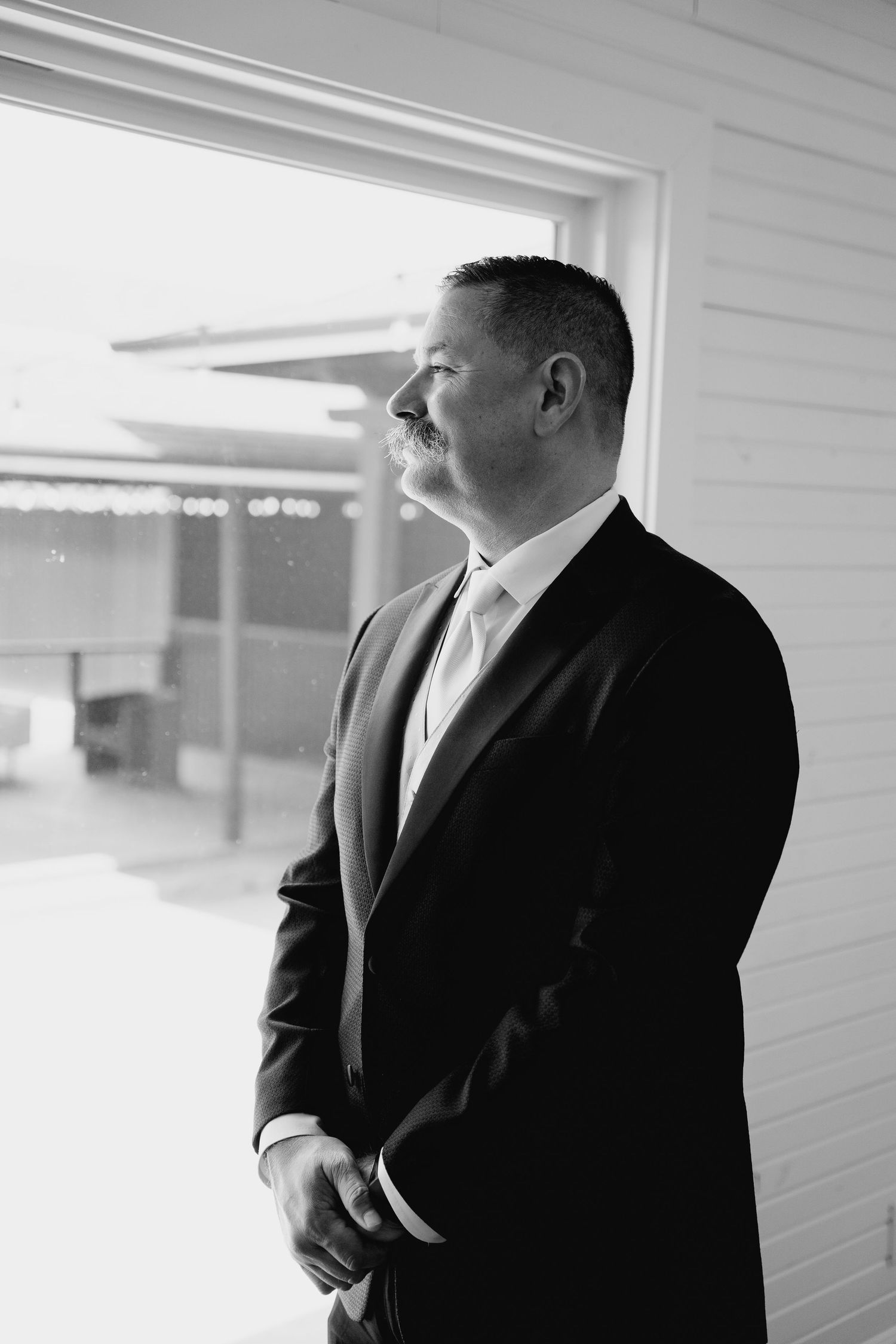 Black and white portrait of a man in a suit with mustache gazing thoughtfully out a window.