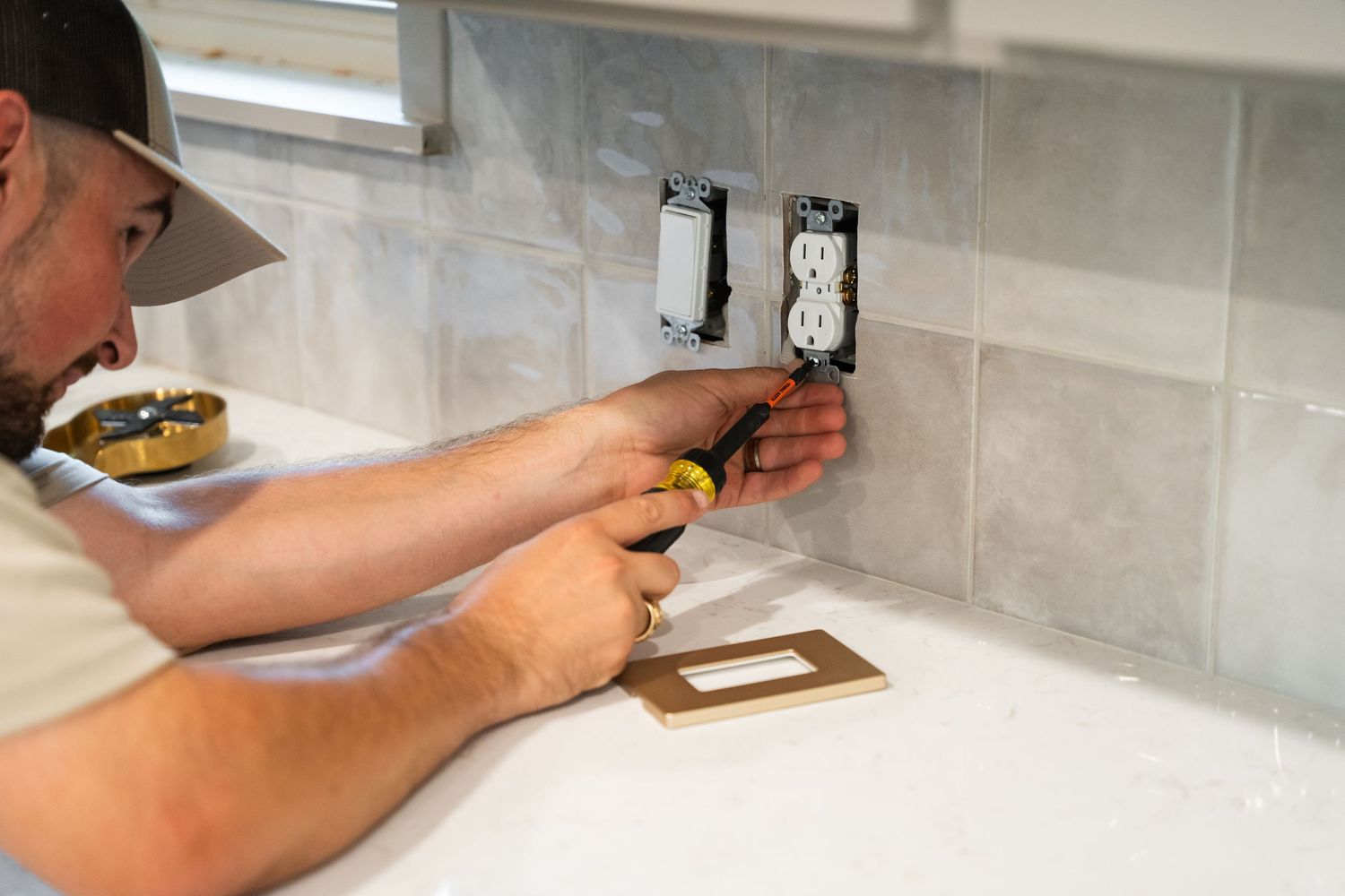 A technician installing electrical outlets on a gray tile kitchen backsplash during home construction.