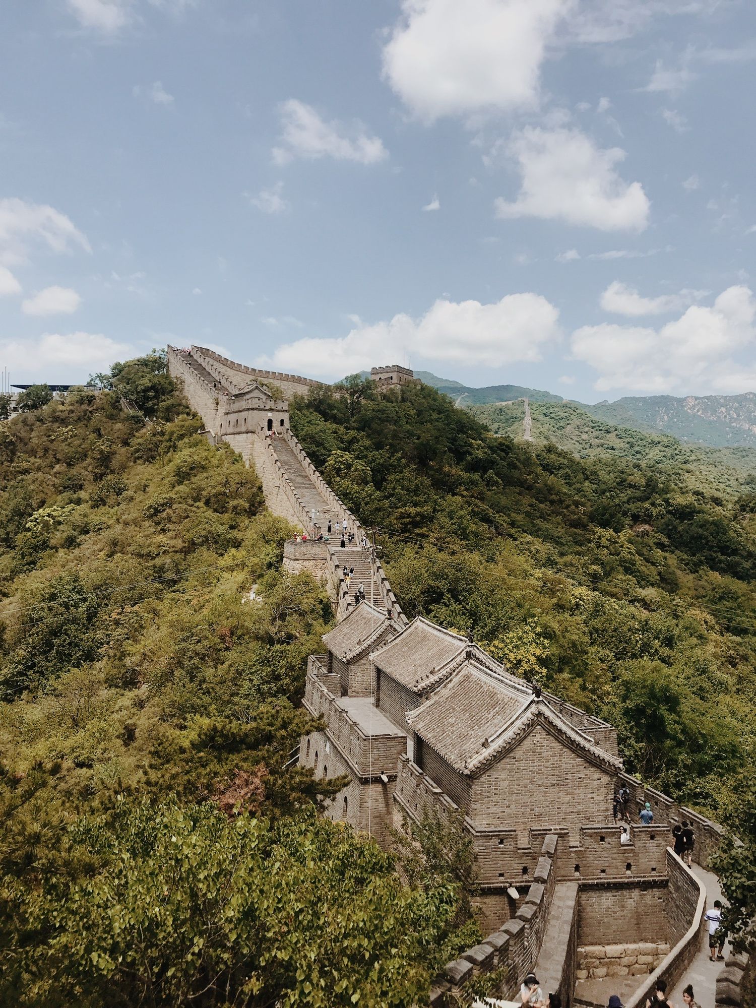 Aerial view of the Great Wall of China winding through lush green mountains under cloudy sky.
