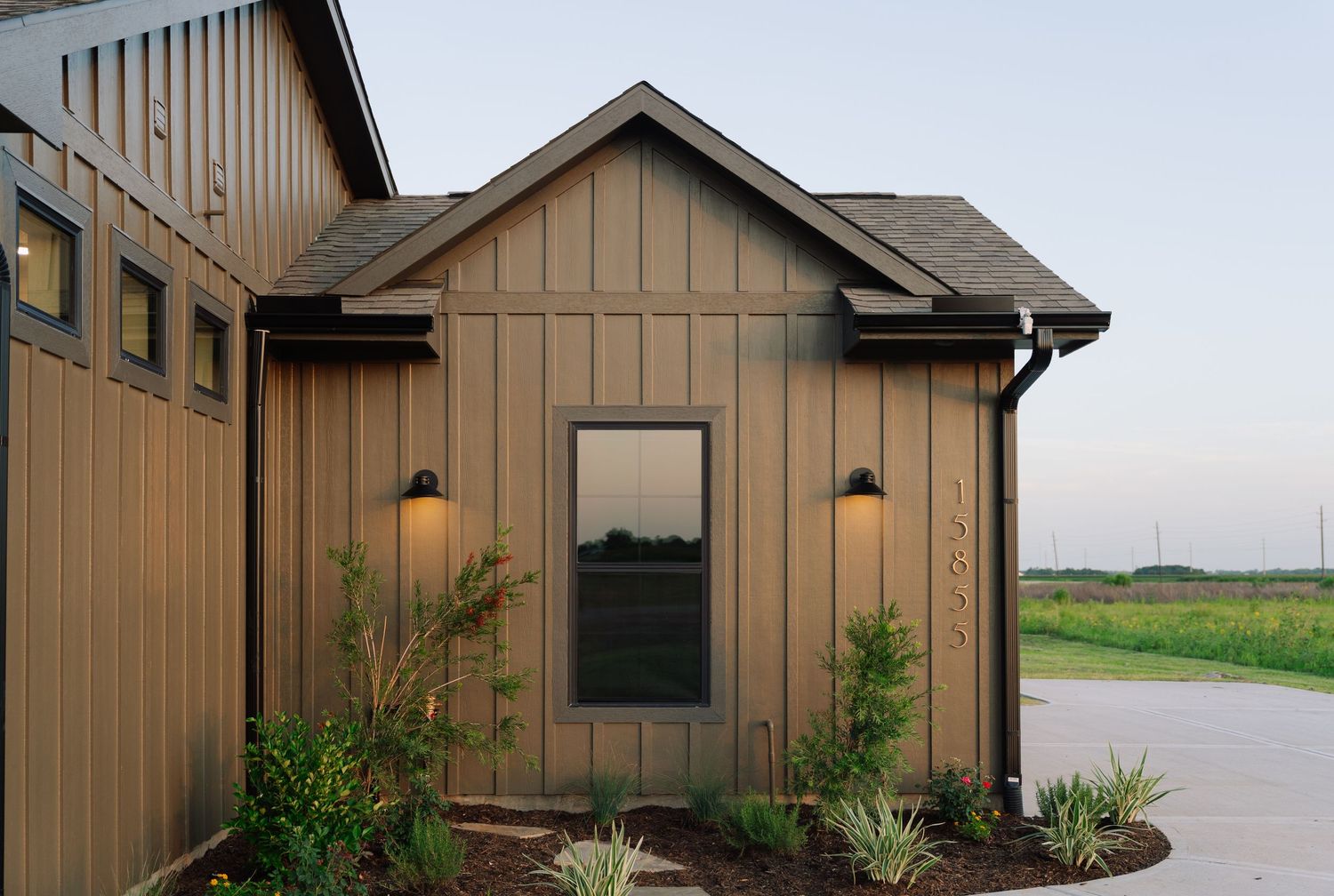 Modern farmhouse exterior with board and batten siding, black wall sconces, and drought-tolerant landscaping.