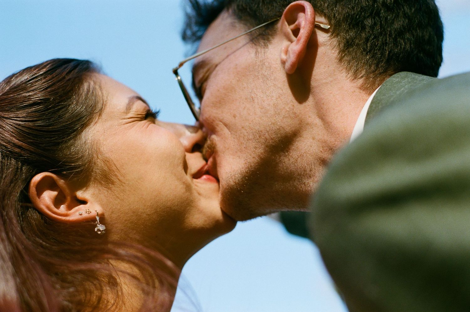 Close-up of a bride and groom sharing a romantic kiss under a blue sky on their wedding day.
