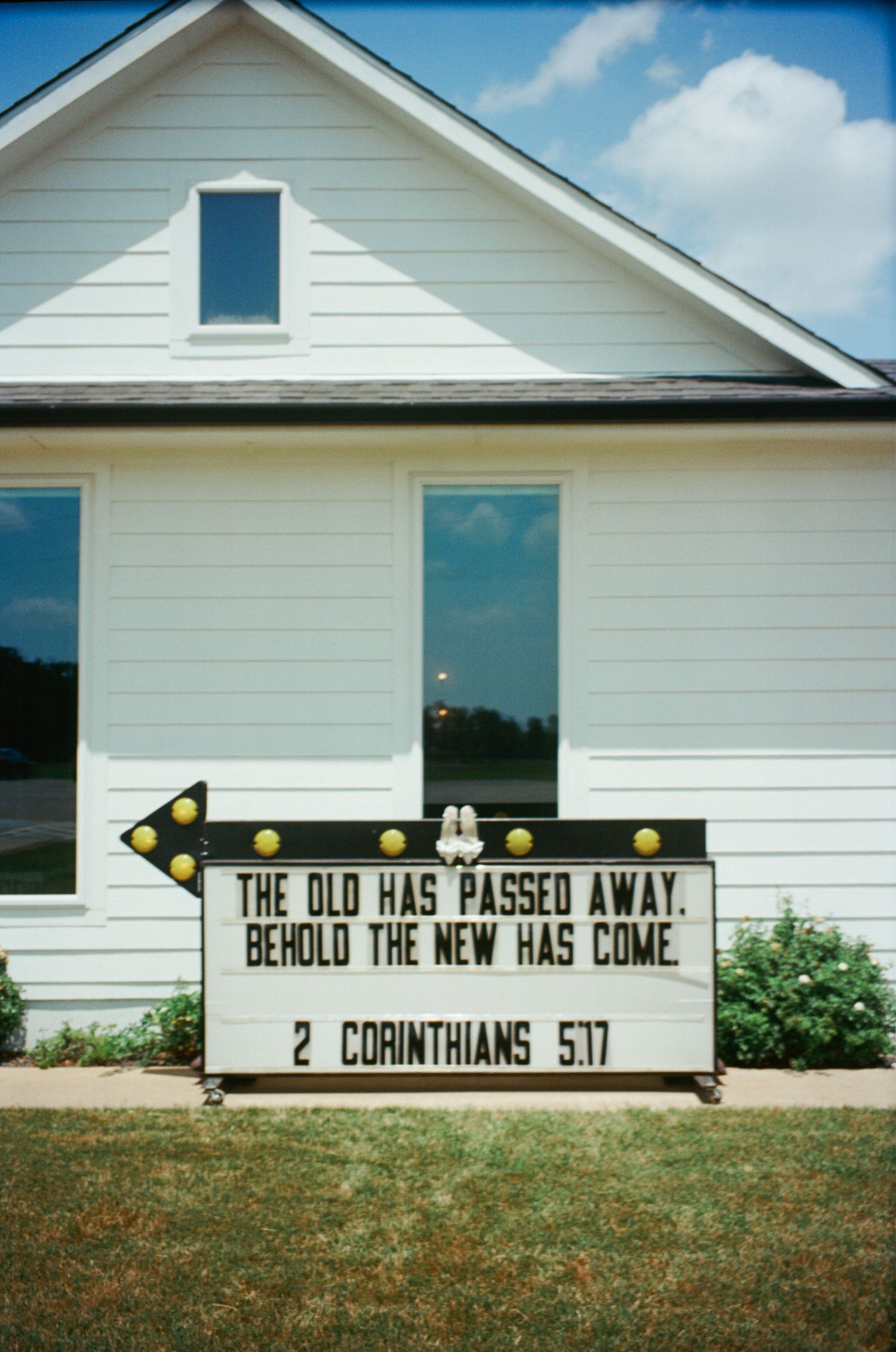 White church exterior with marquee sign displaying 2 Corinthians 5:17 Bible verse on sunny day.