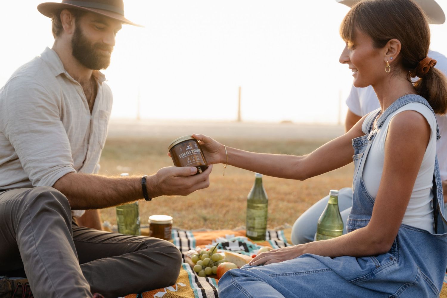 Couple sharing a drink at an outdoor picnic during golden hour sunset.