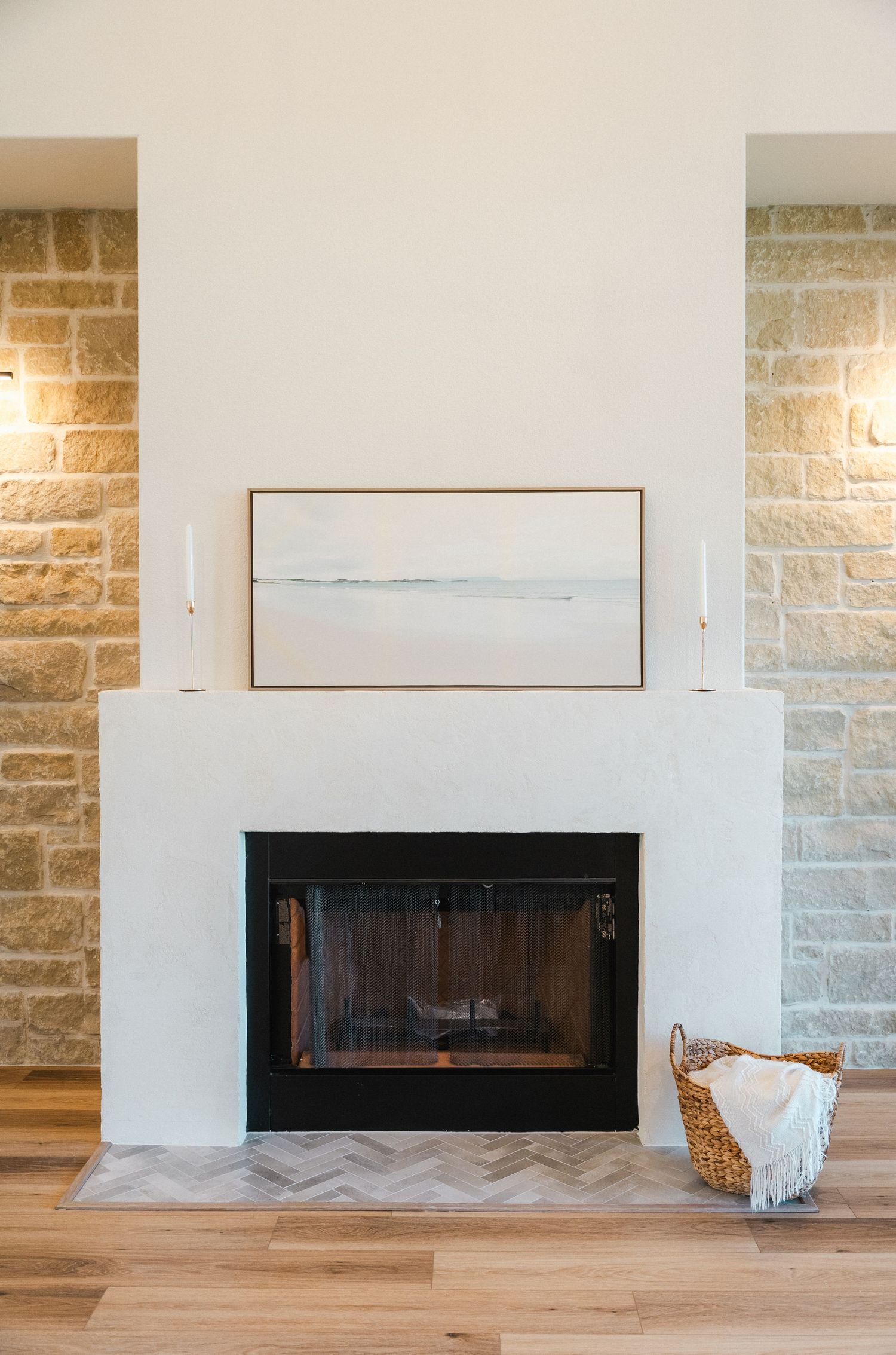 White plaster fireplace with black surround, herringbone tile hearth, and limestone accent walls in living room.