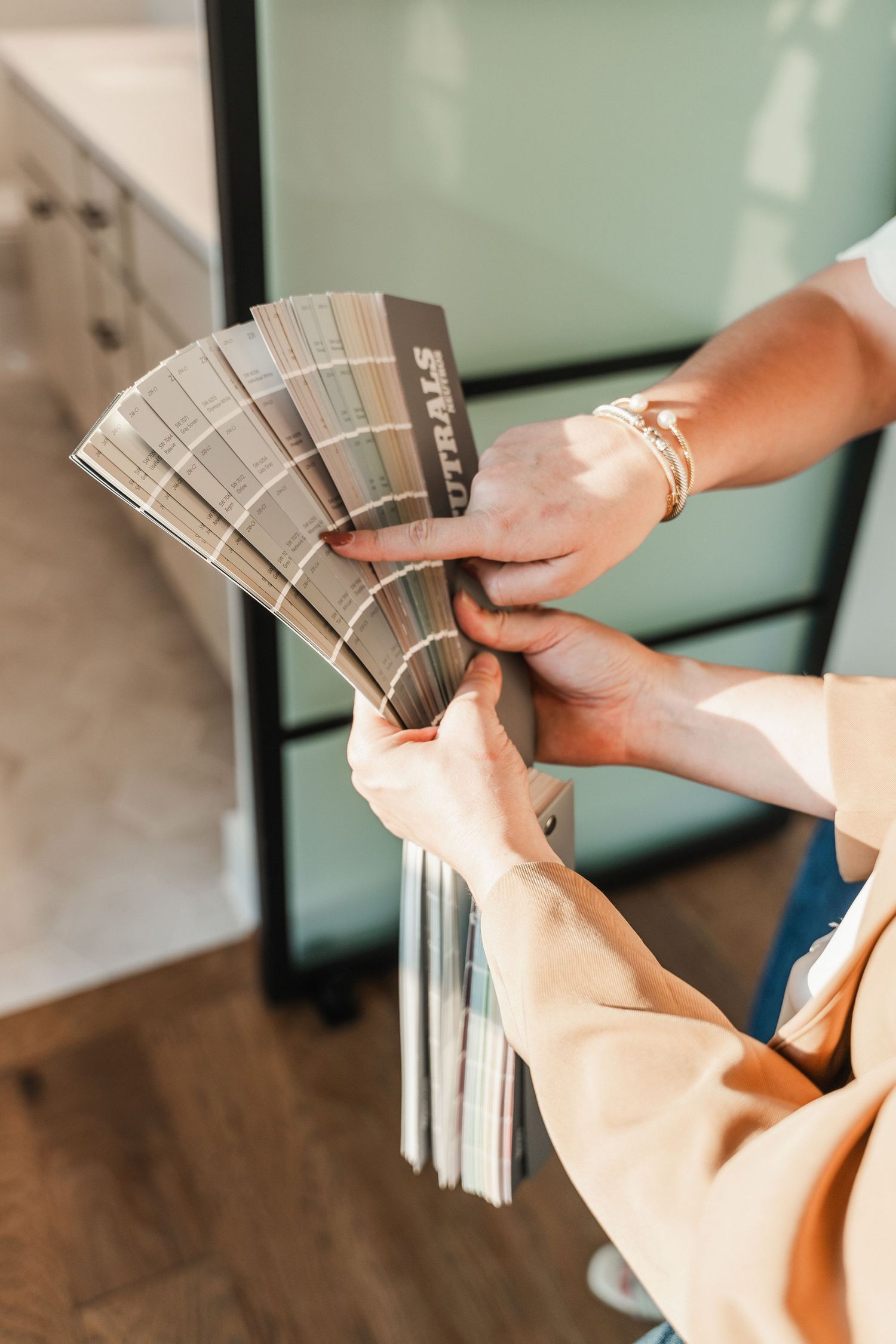 Person holding a fan of neutral paint color swatches for interior design selection.