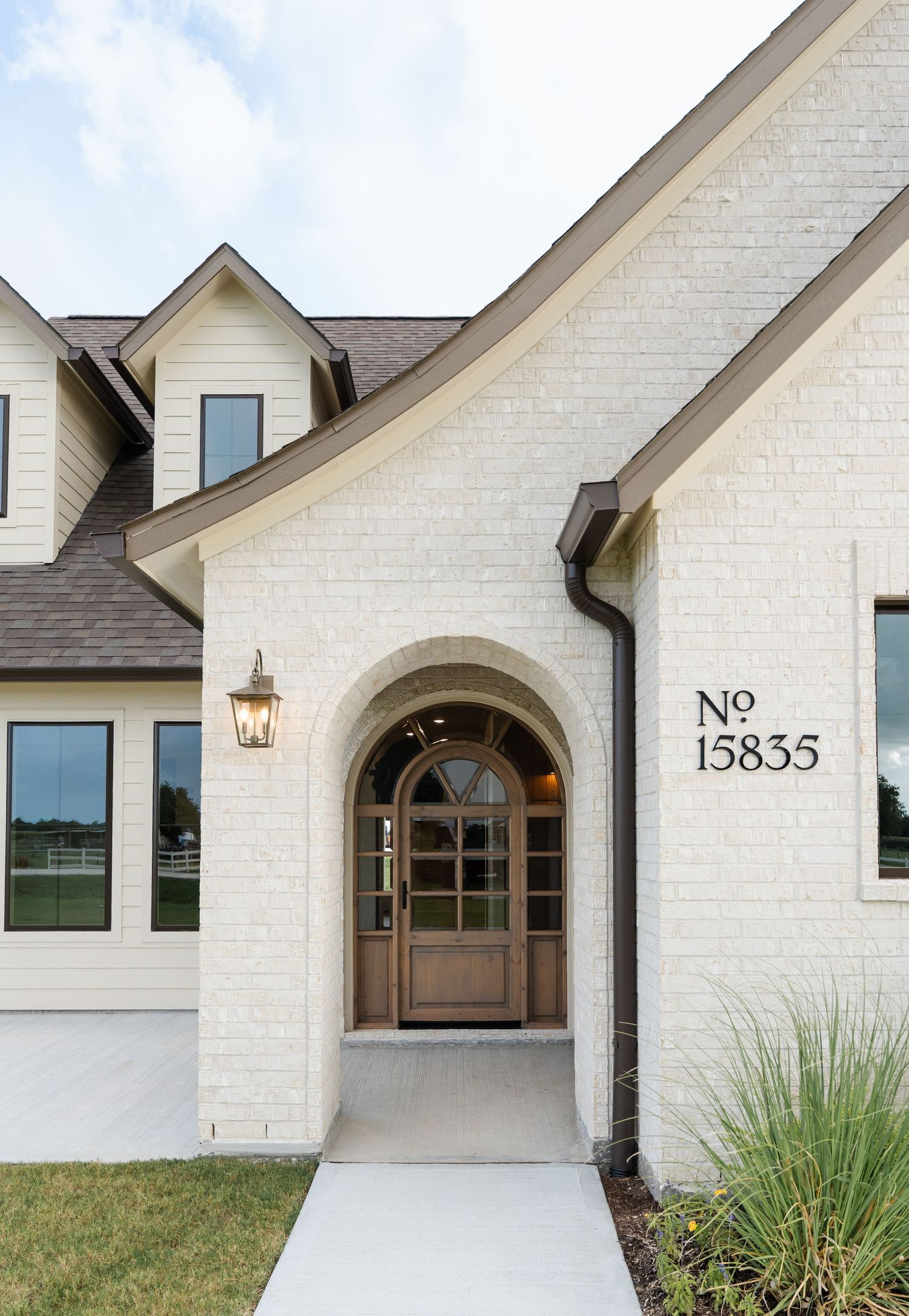 White painted brick home exterior with arched wood front door and address number 15835 on wall.